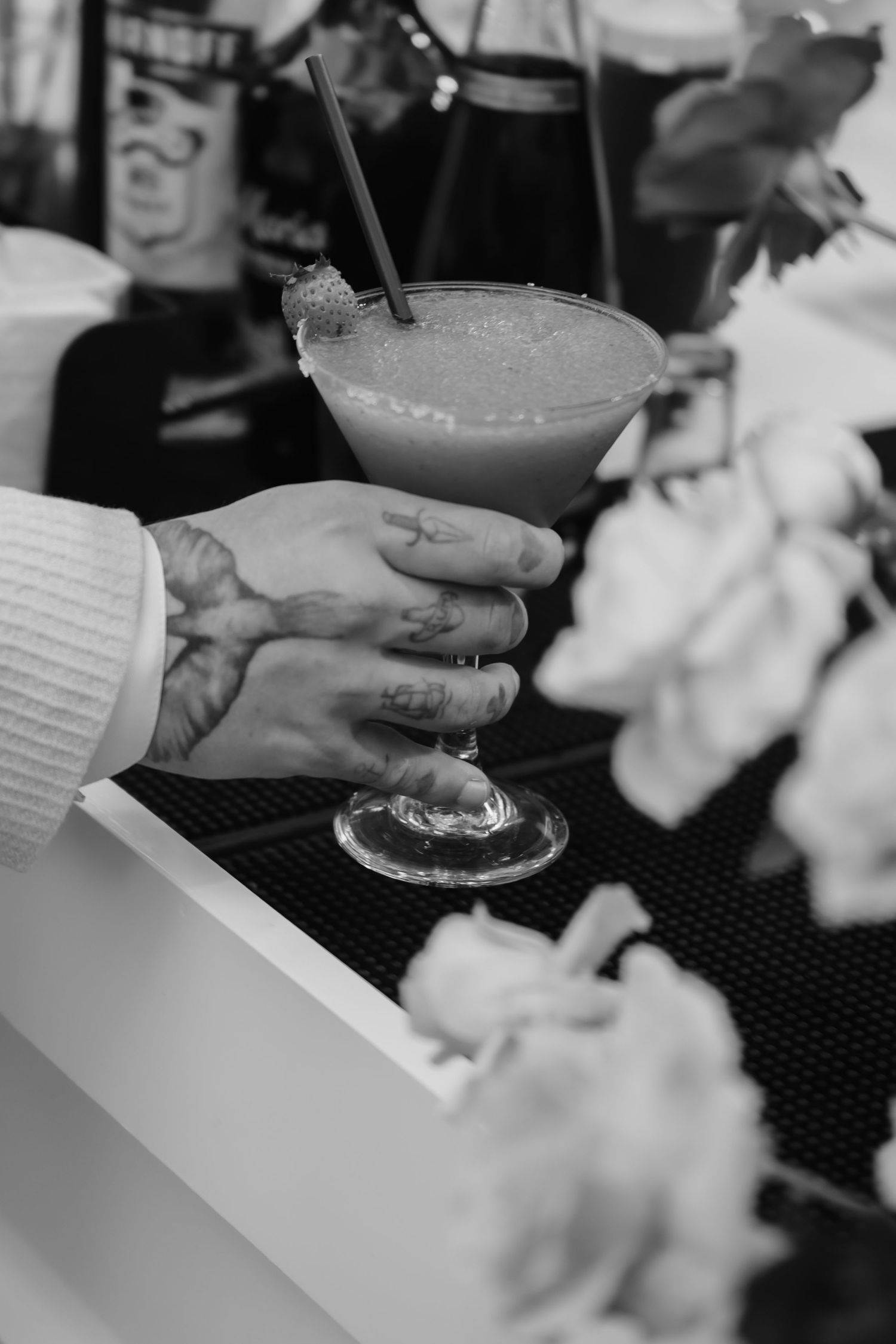 Black and white photo of tattooed hands holding a margarita cocktail at a wedding bar.