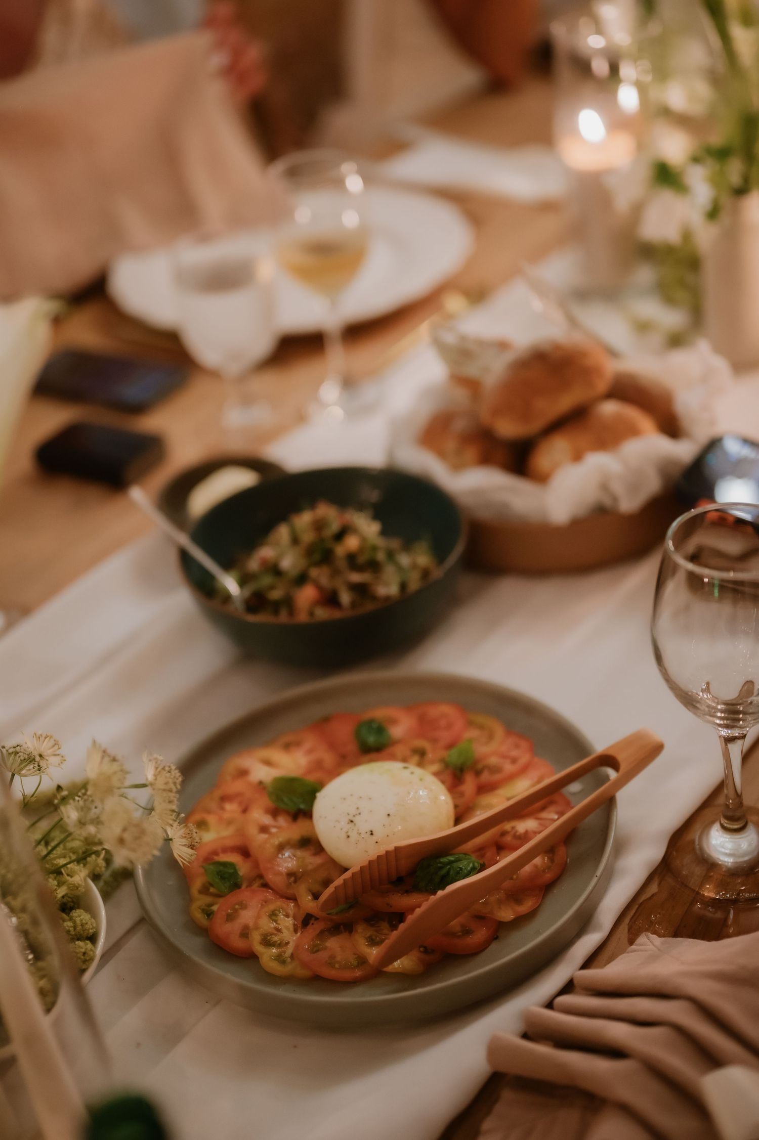 Wedding reception dinner table with caprese salad, bread basket, and white wine glasses.