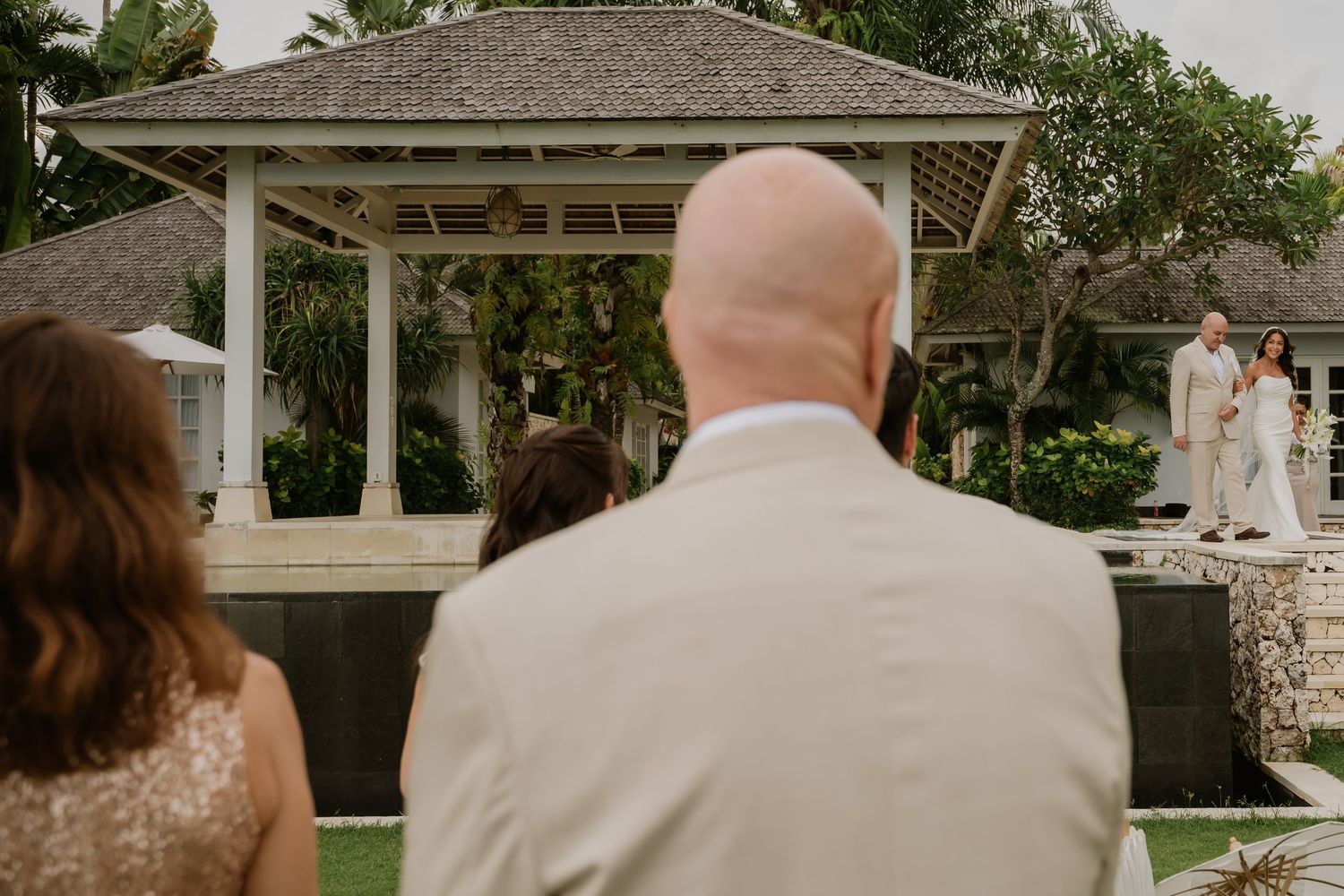 Guests watch bride and groom exchange vows at outdoor tropical wedding ceremony.
