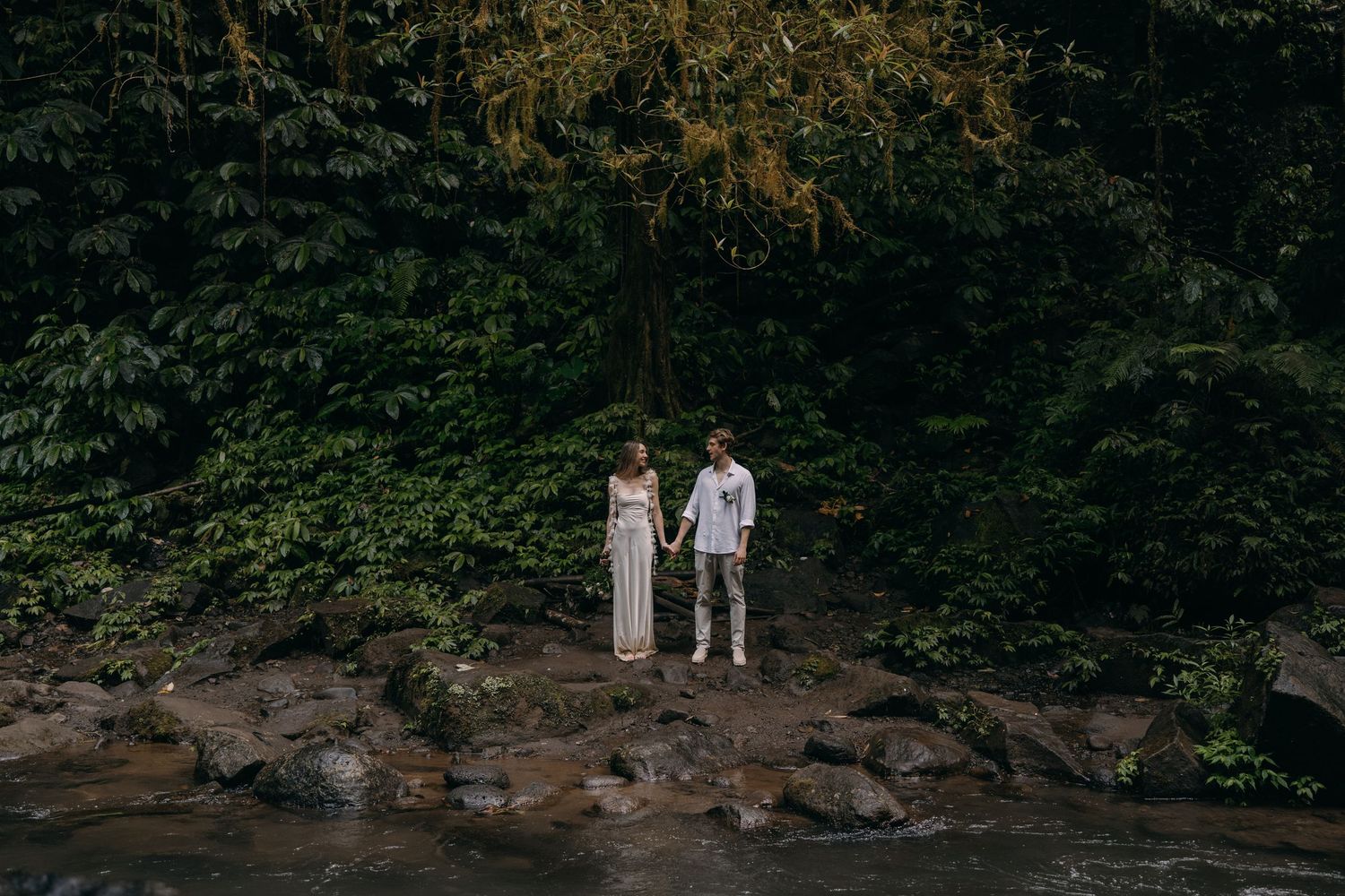 A couple walks along a scenic rocky stream surrounded by lush green forest during a peaceful outdoor excursion.
