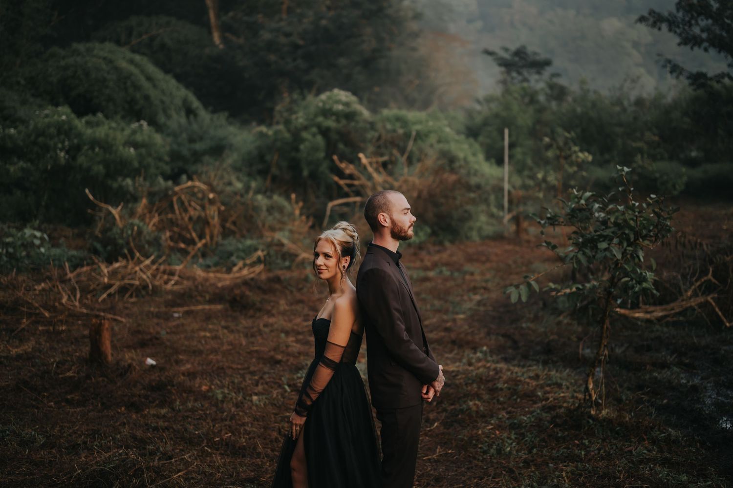 A series of moody forest engagement photos showing a couple embracing among tall trees at sunset.