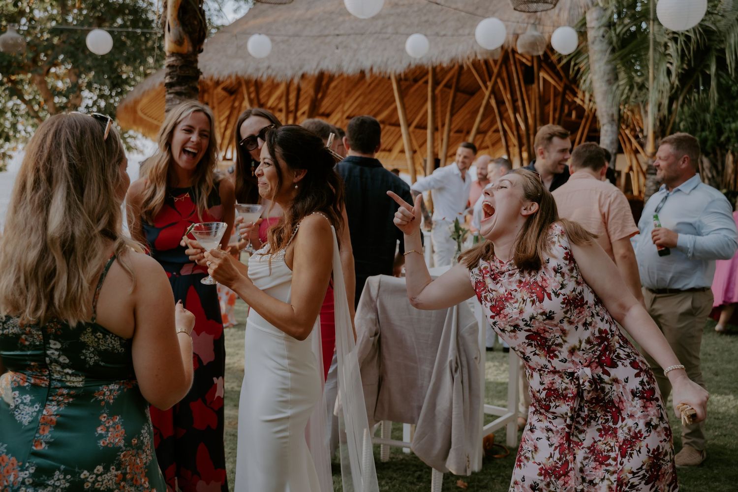 Wedding guests dancing and celebrating at an outdoor reception with white paper lanterns and string lights.
