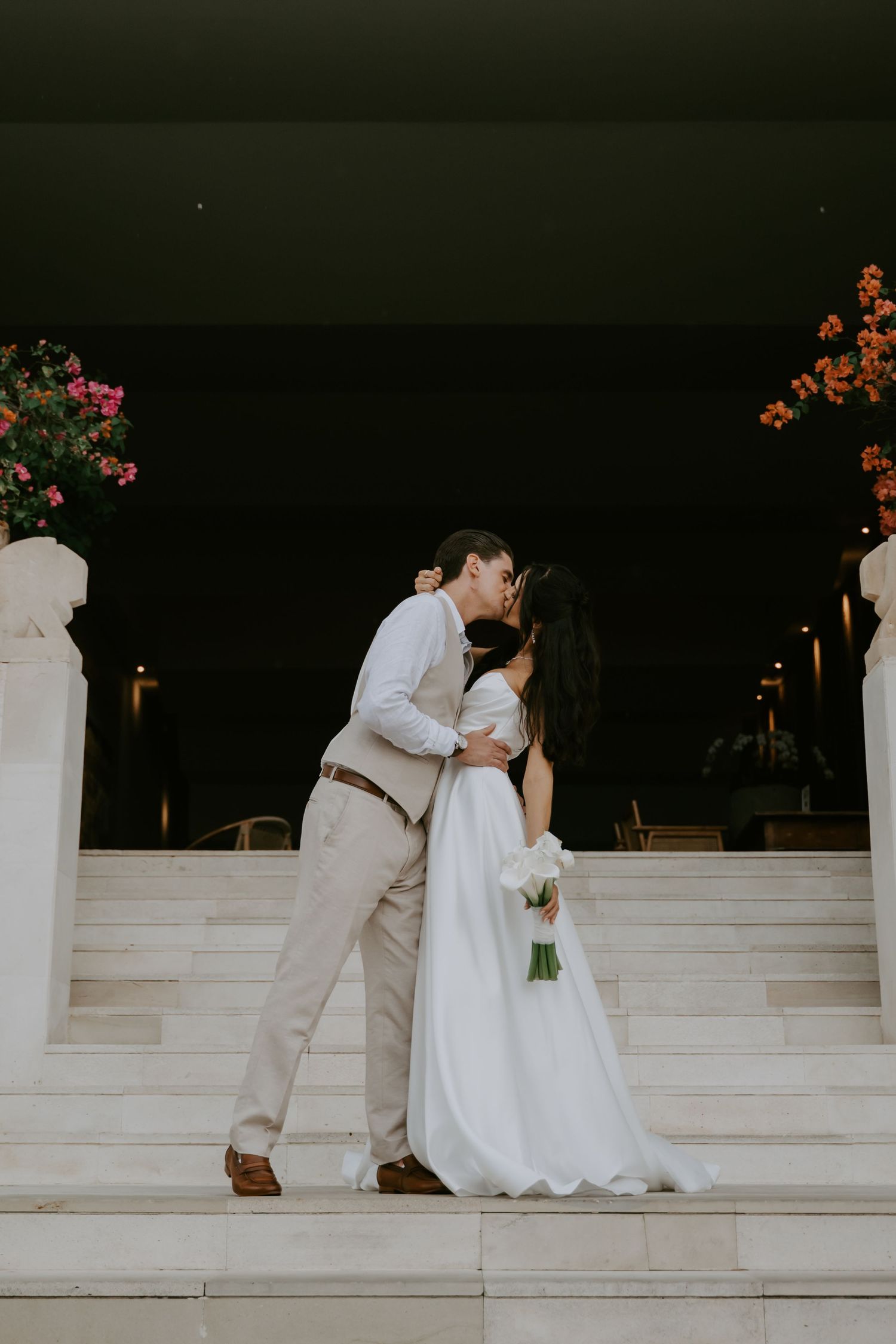 Newlyweds share romantic moments on white marble steps at dusk.