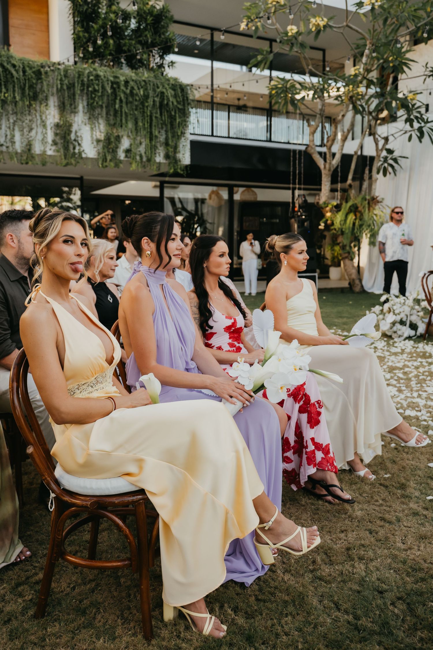 Wedding guests in colorful dresses seated outdoors during garden ceremony.