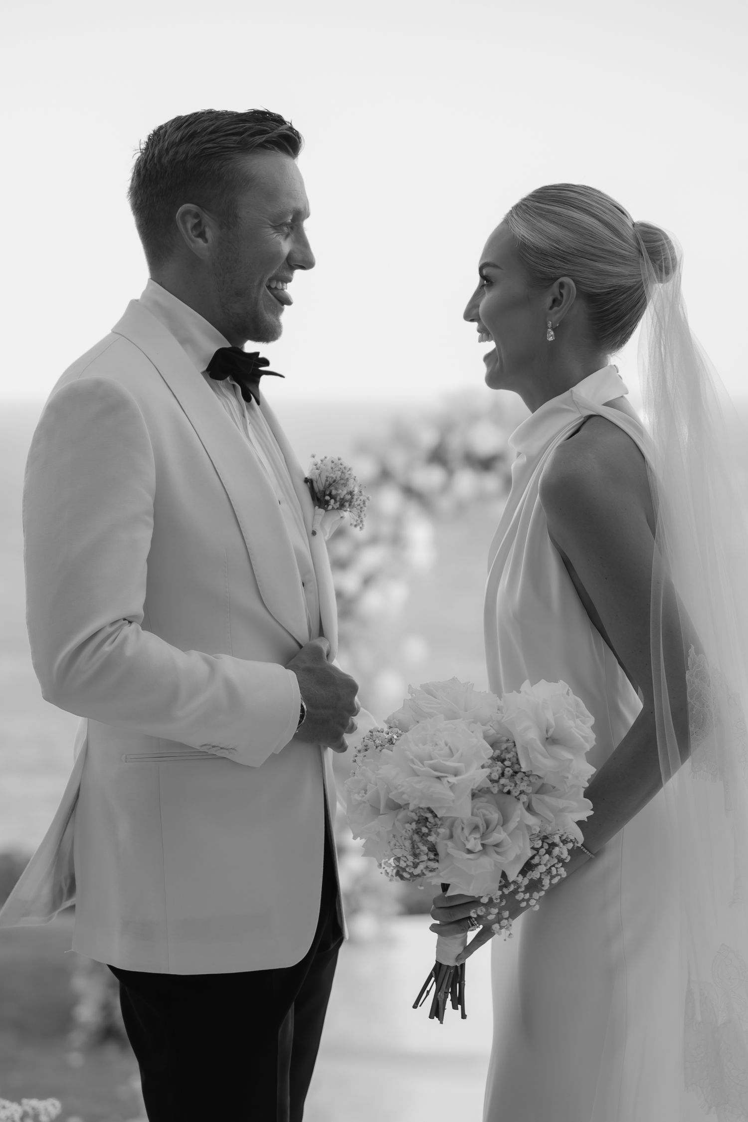Elegant black and white portrait of couple in formal wedding attire against bright background.