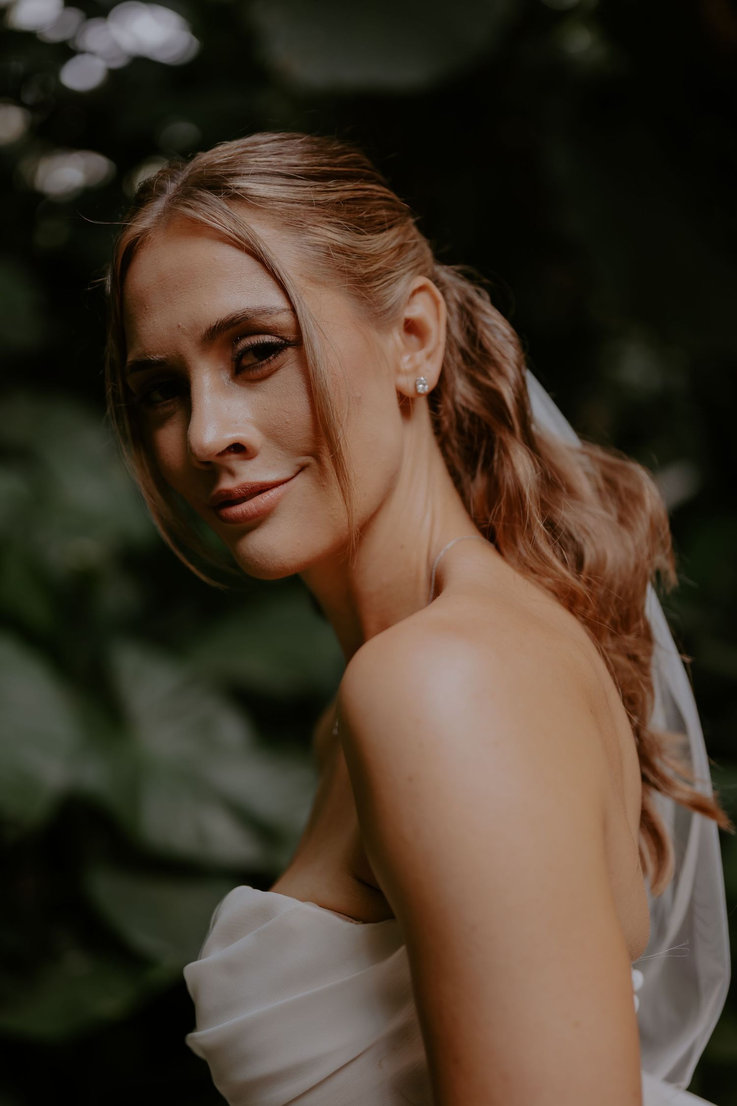 Artistic close-up portrait of a bride in a white wedding dress against a dark natural background.