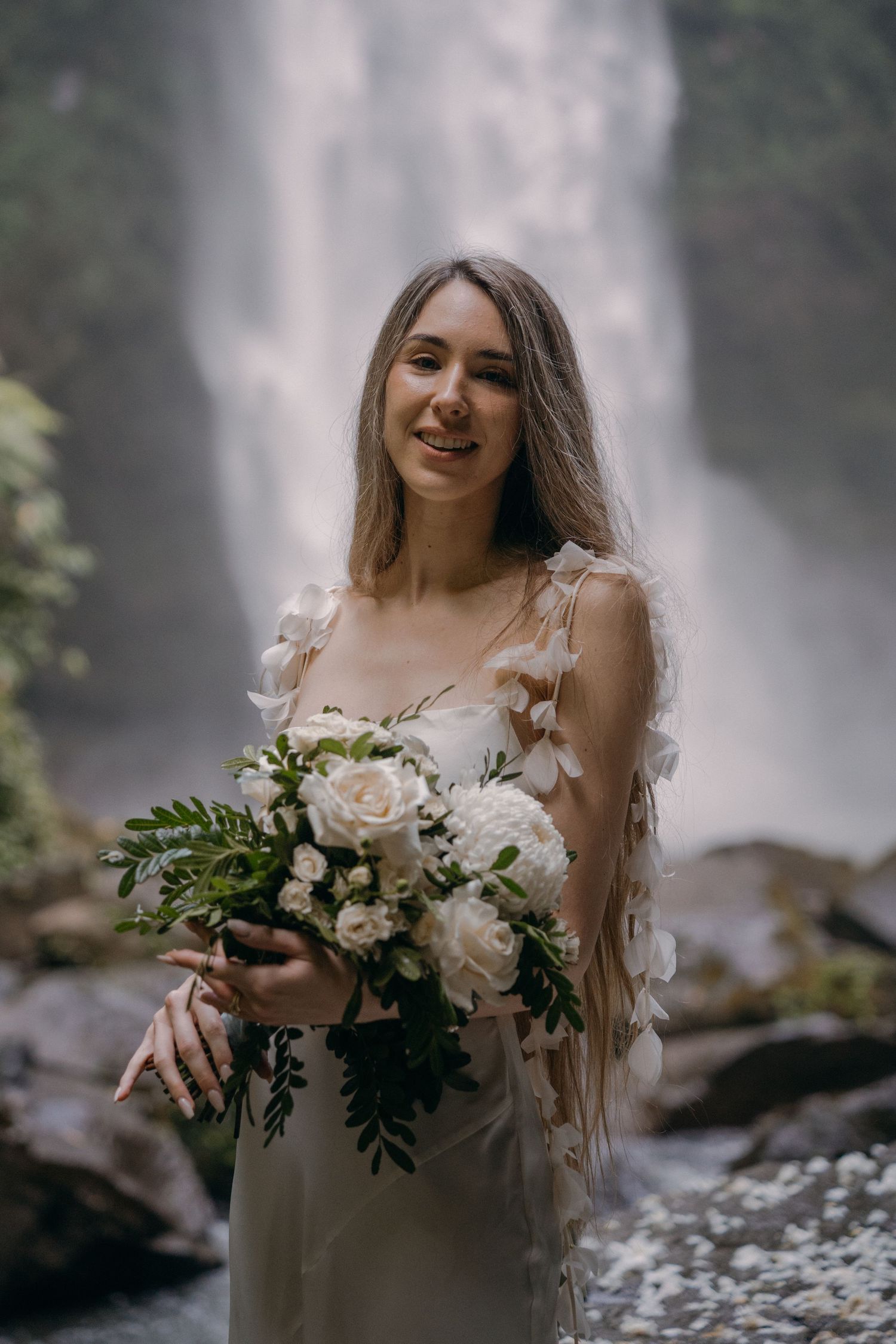 A romantic bridal portrait series with white floral bouquet against misty waterfall backdrop in nature.