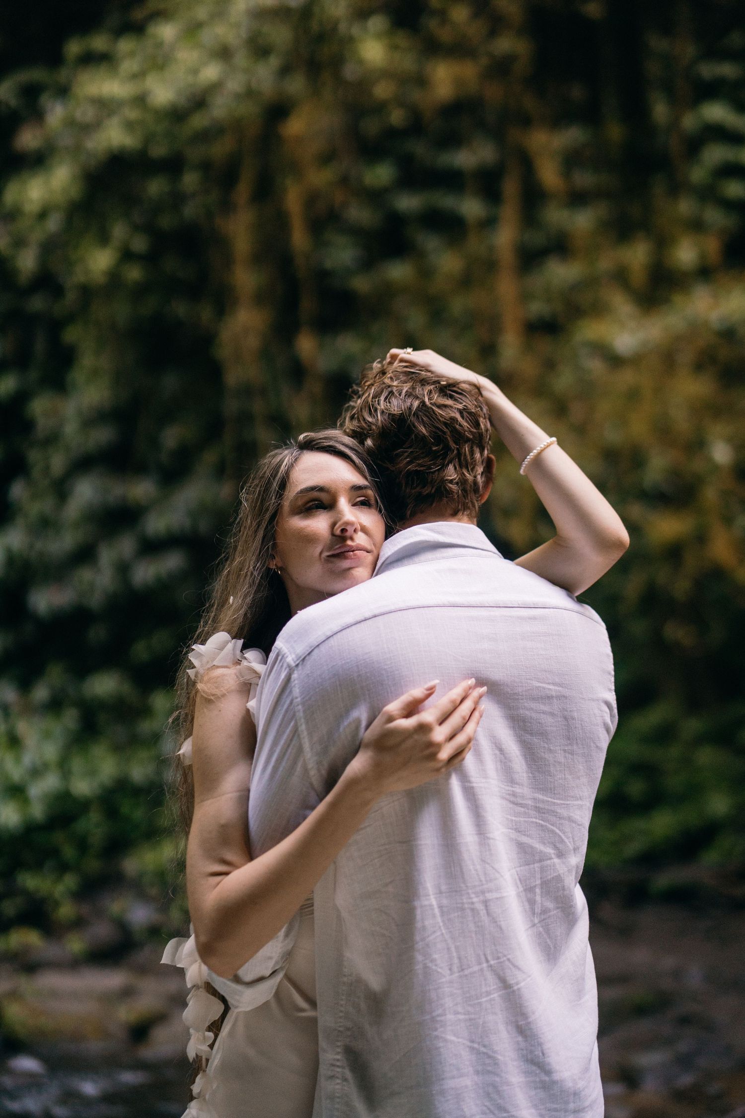 A couple embraces intimately in an outdoor setting with autumn trees in the background.