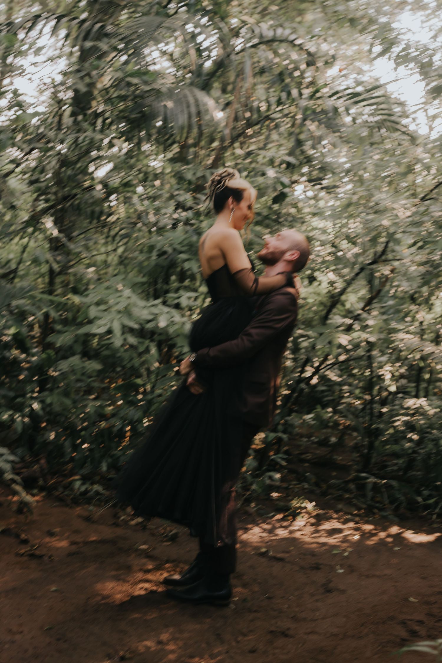 A romantic embrace captured in a wooded setting with natural lighting.