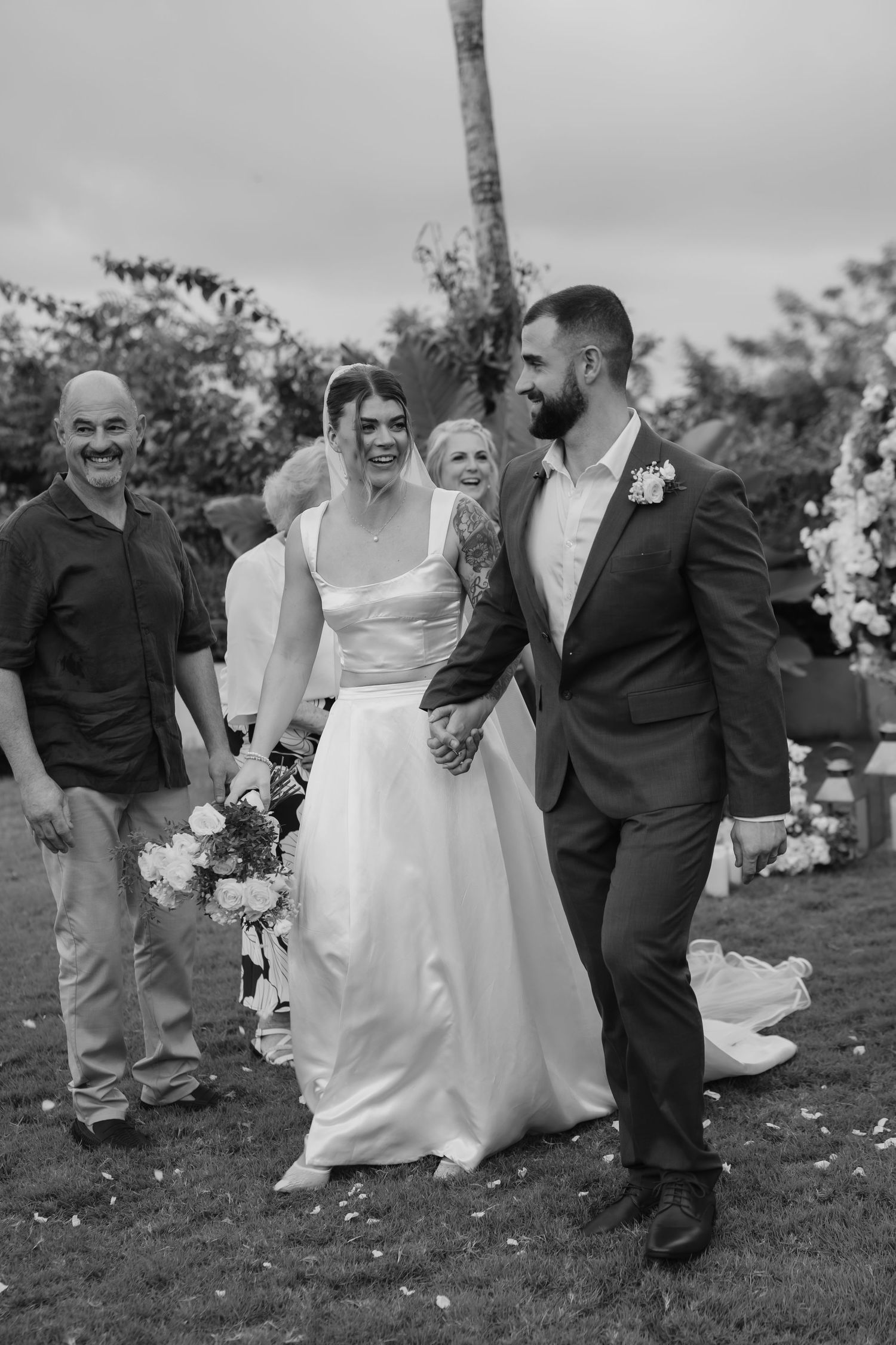 Black and white photo of newlyweds walking down the aisle hand in hand after outdoor wedding ceremony.