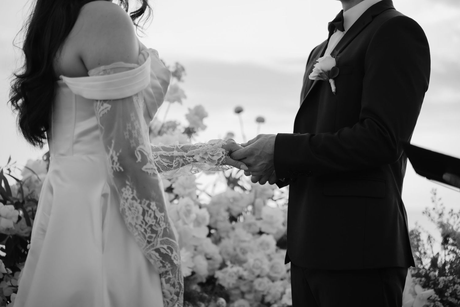 Black and white photo of bride and groom exchanging rings at floral wedding altar.