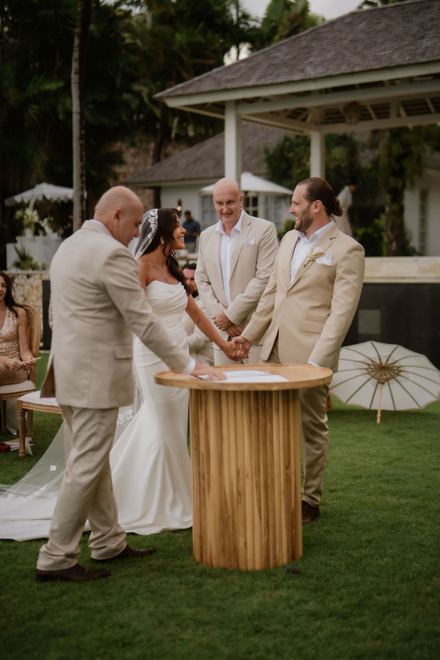 Bride and groom sign marriage certificate at wooden table during outdoor garden wedding ceremony.