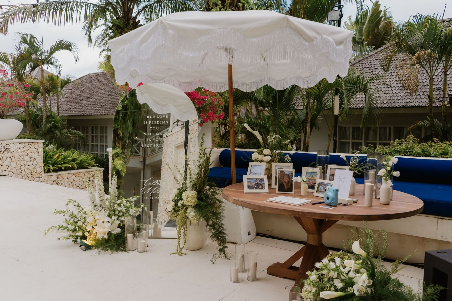 Romantic outdoor wedding decor with white umbrella, floral arrangements, candles, and a wooden table.
