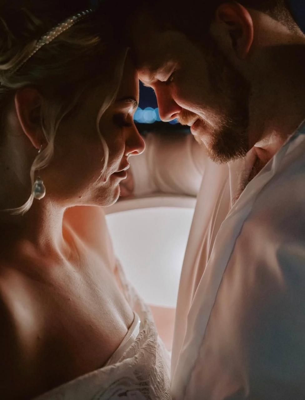 Intimate close-up portrait of a couple in wedding attire with dramatic lighting.