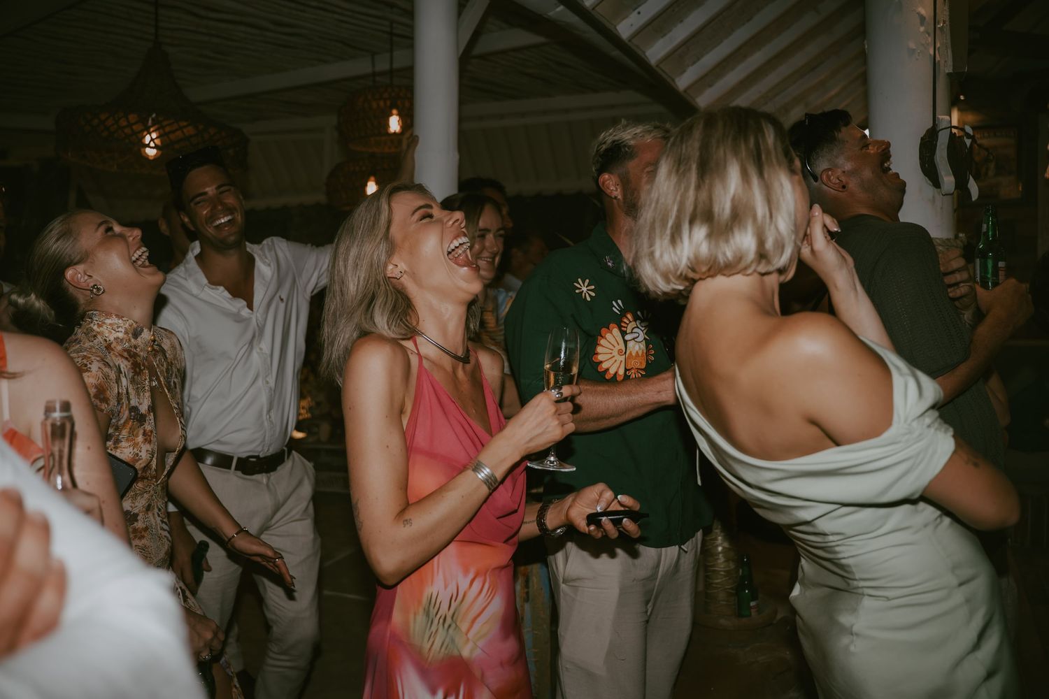 Lively dance floor scene at wedding reception with guests dancing under dim lighting.