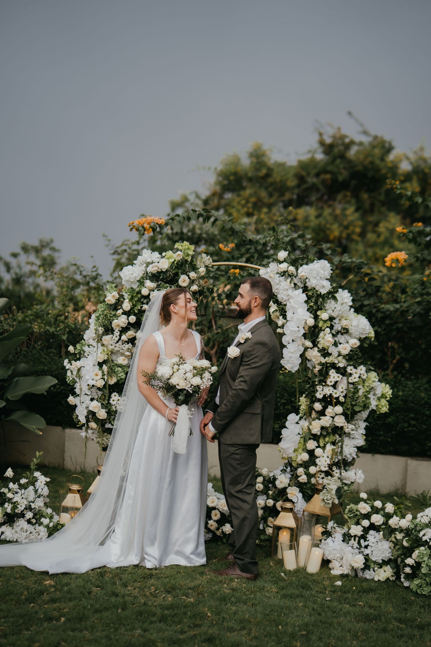 Bride and groom exchange vows under white floral circular wedding arch.