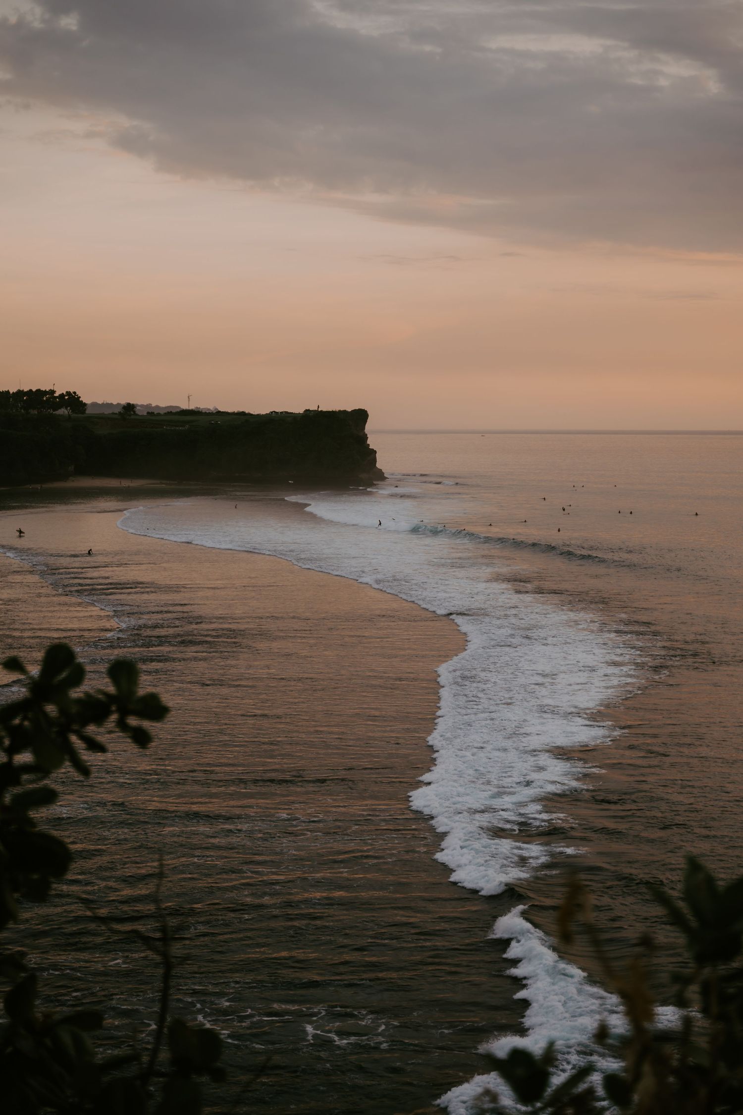 Stunning sunset view of a curved beach with gentle waves and dramatic cliffs.