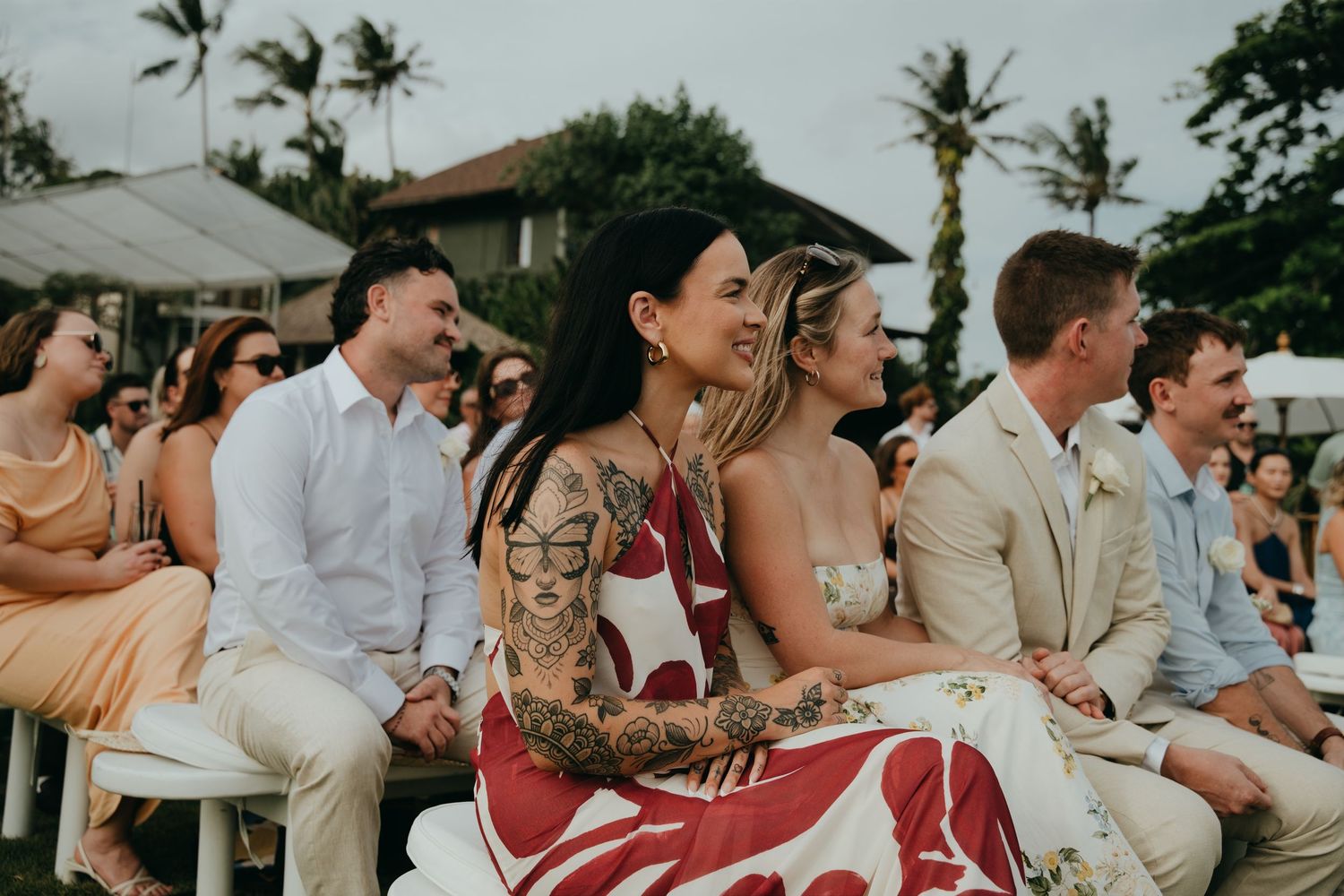 Wedding guests seated at an outdoor ceremony, including a woman with floral tattoos.