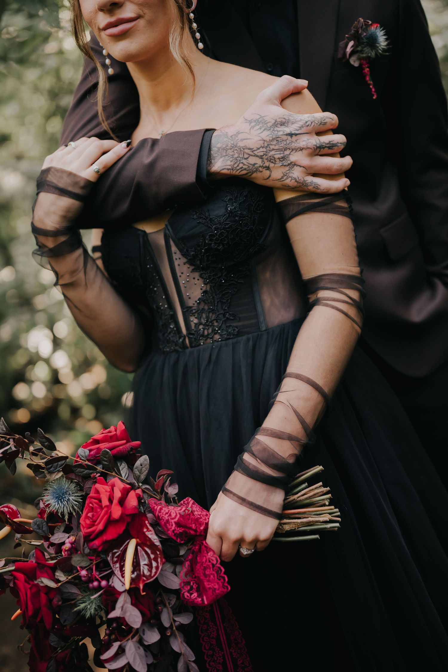 Close-up details of black formal wear and a dramatic deep red and burgundy wedding bouquet.