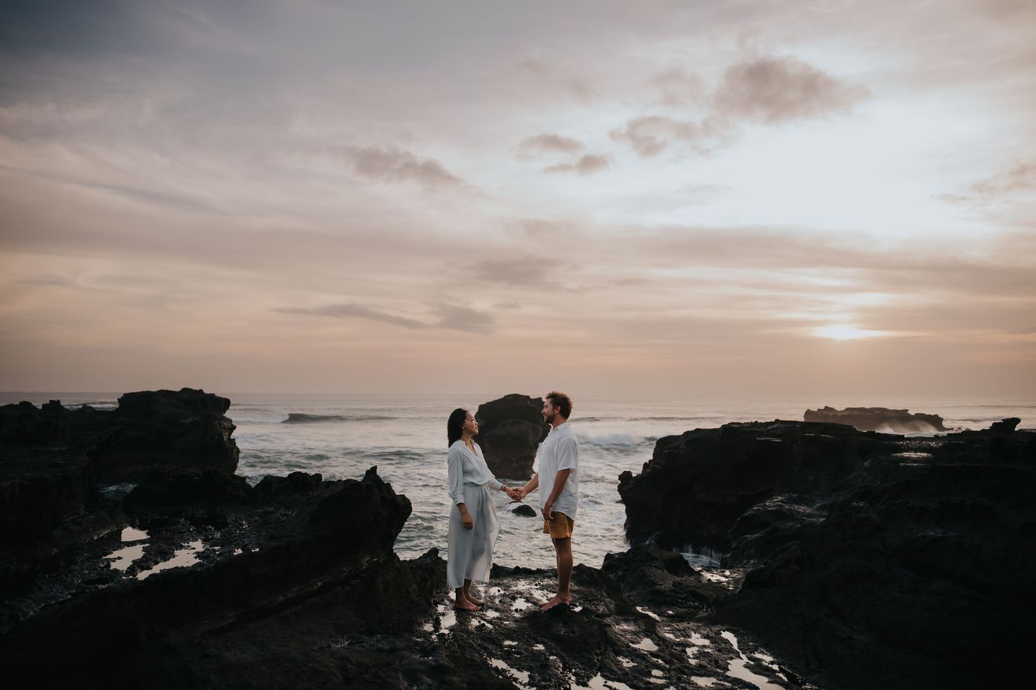 Dramatic coastal landscape at sunset with silhouetted cliffs and waves crashing against rocky shoreline.