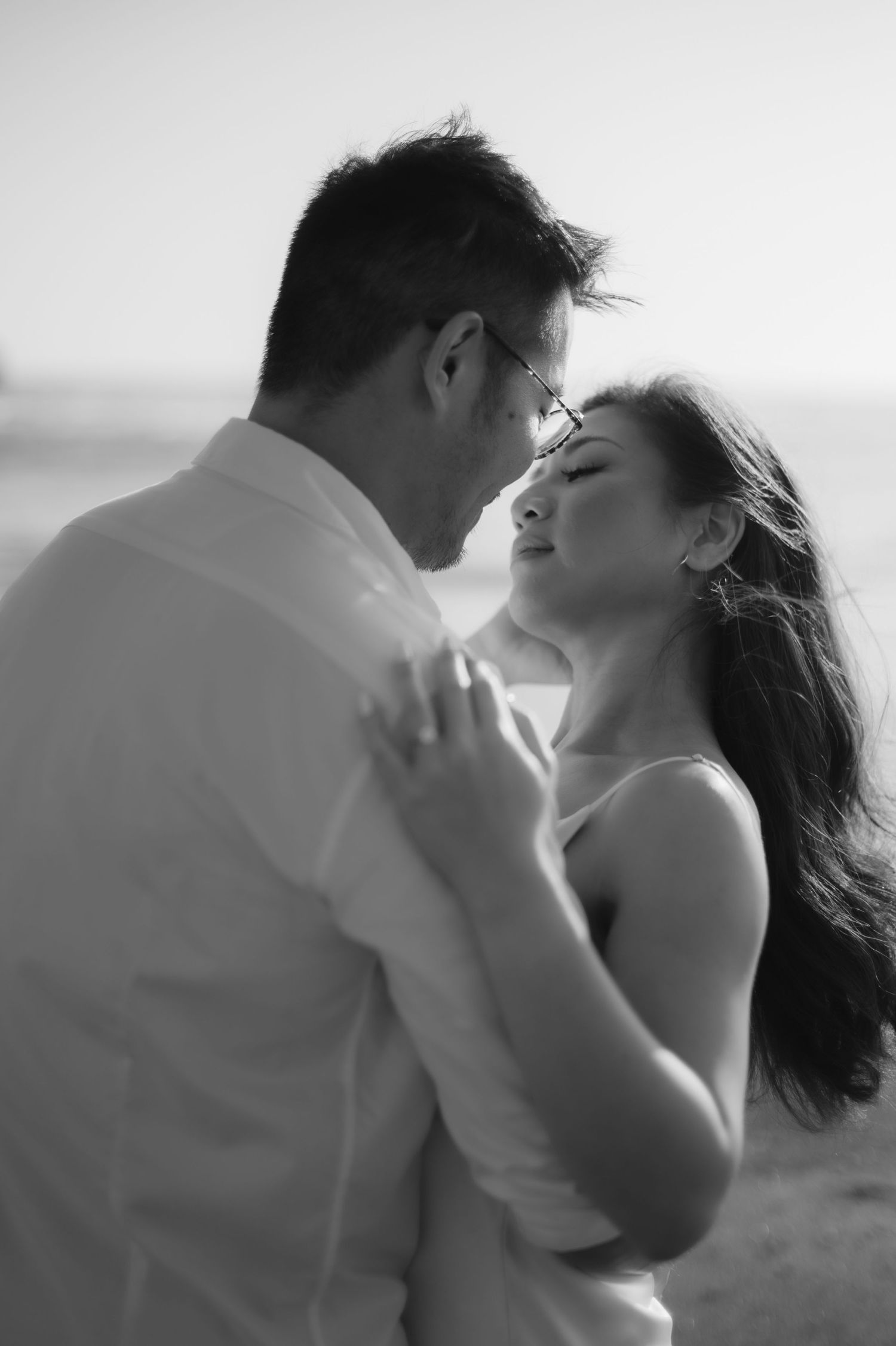 Black and white photo of a romantic couple embracing closely on a beach, woman with eyes closed leaning toward man.