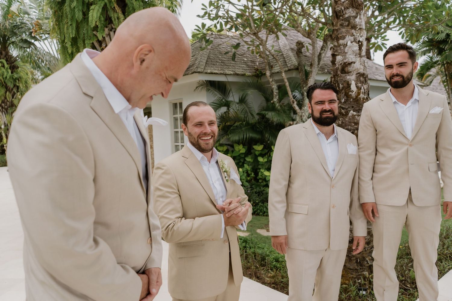 Groomsmen in matching tan suits sharing a joyful moment outdoors before the wedding ceremony.