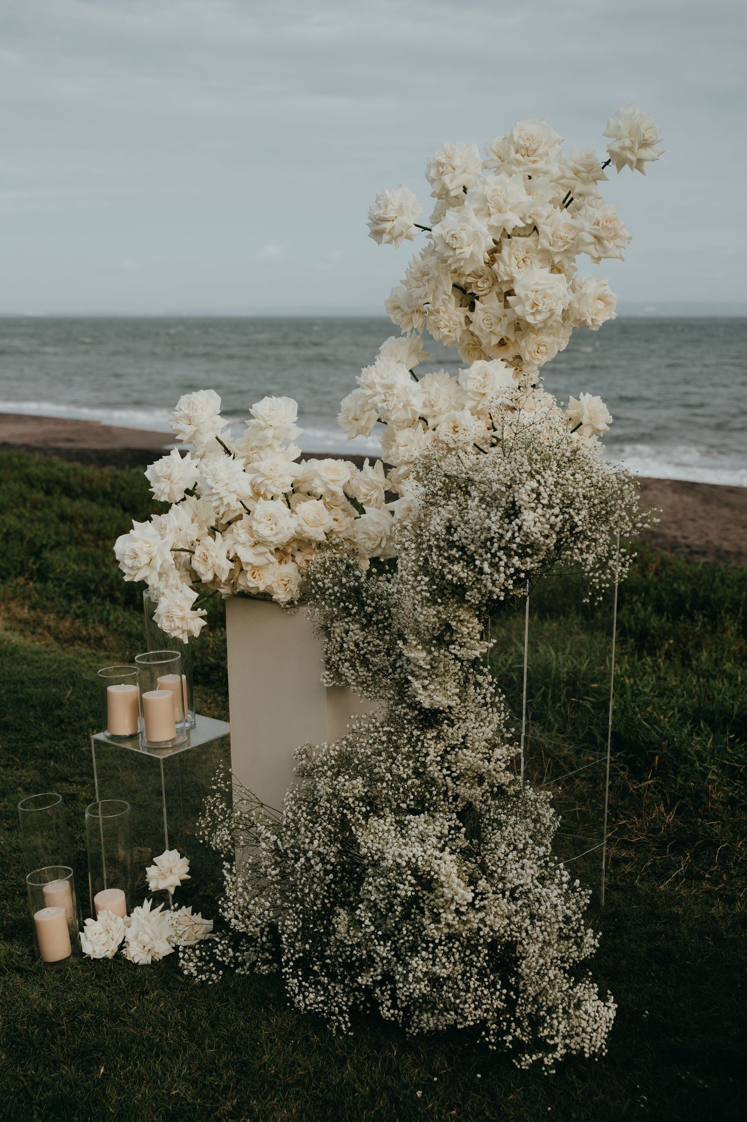 Elegant outdoor wedding ceremony arch with white roses and baby's breath beside the ocean.