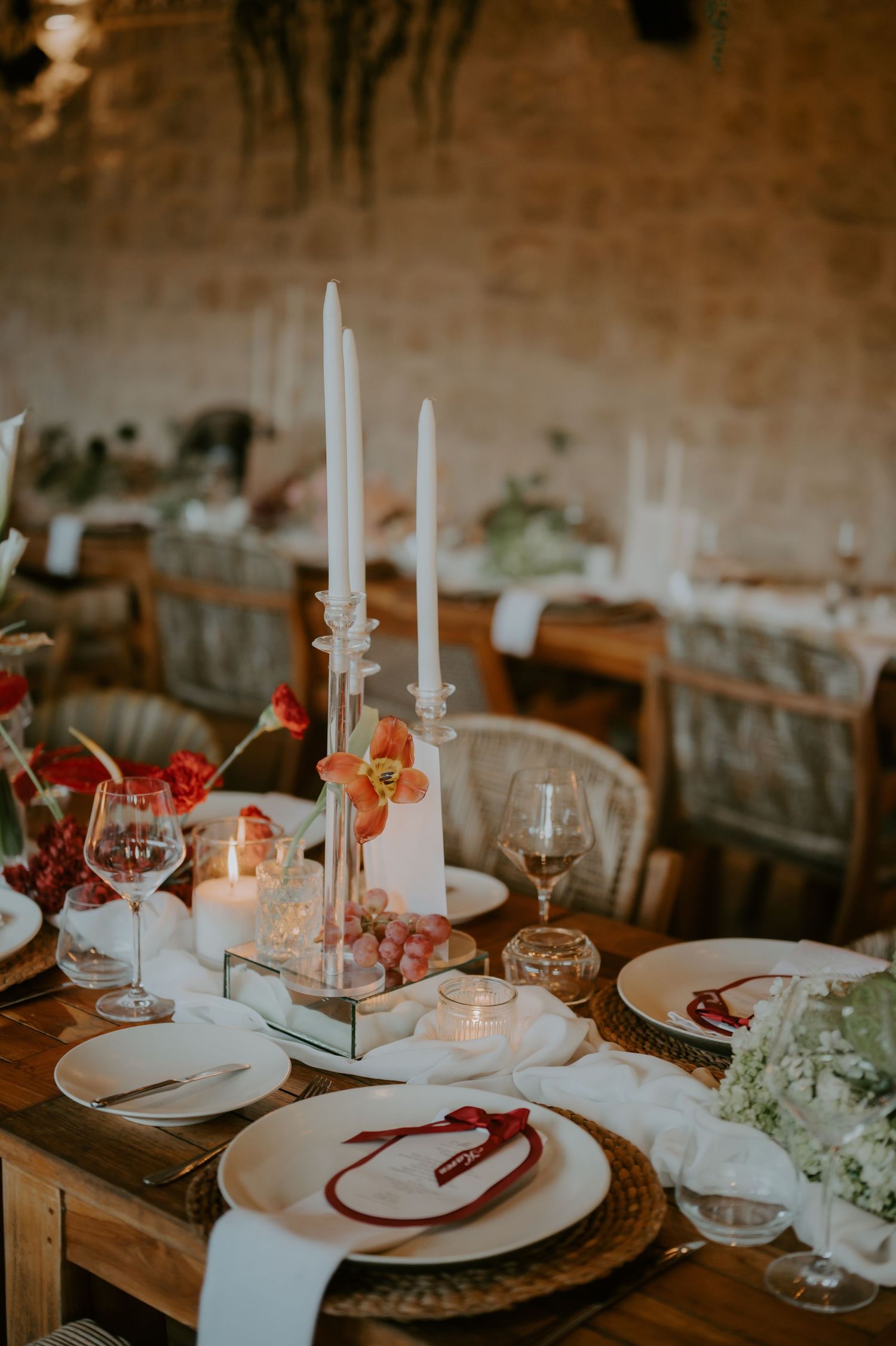 Elegant wedding reception table setting with white taper candles, floral arrangements, and fine dinnerware on rustic wood.