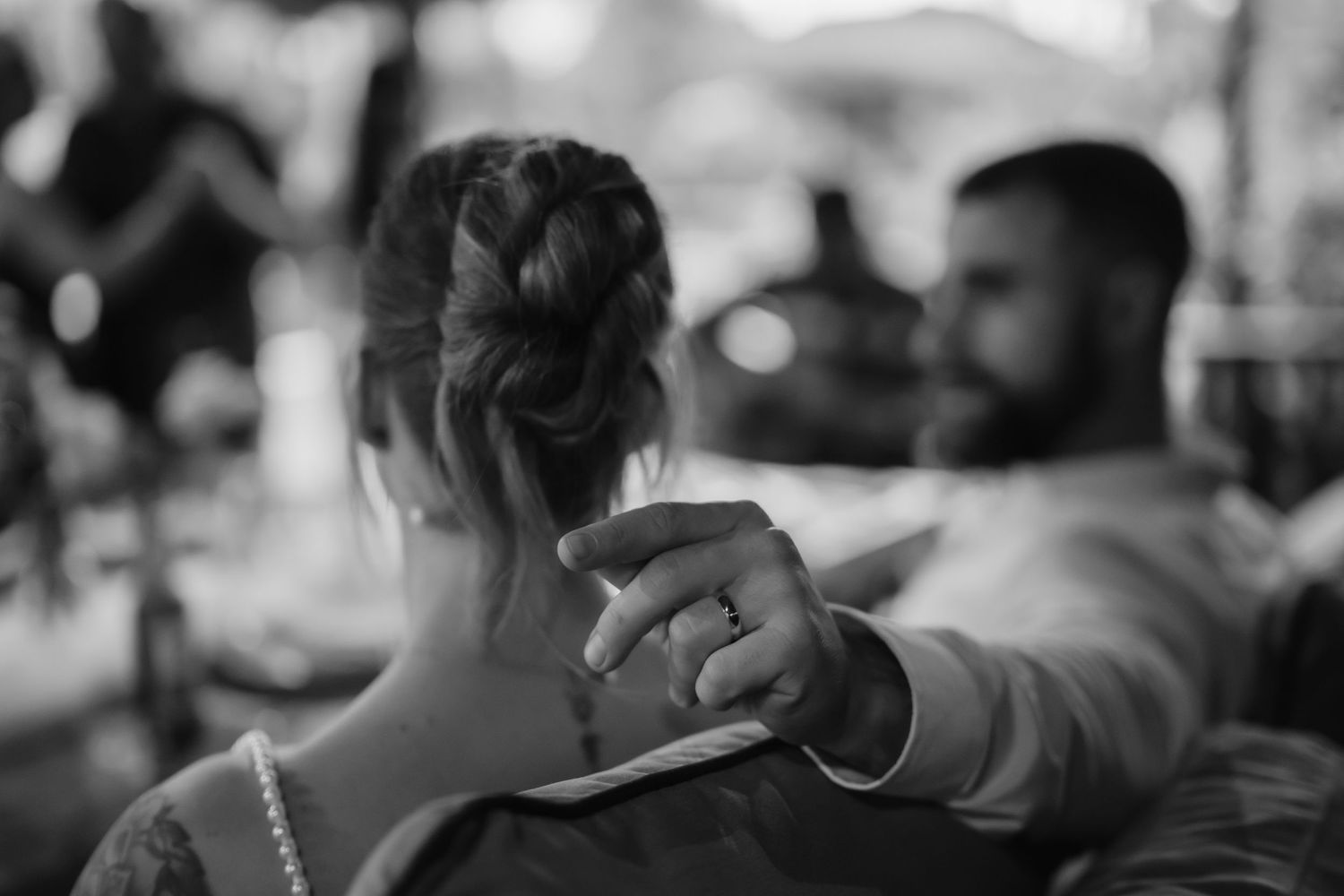 Black and white photo of groom touching brides updo hairstyle with wedding ring visible at reception.
