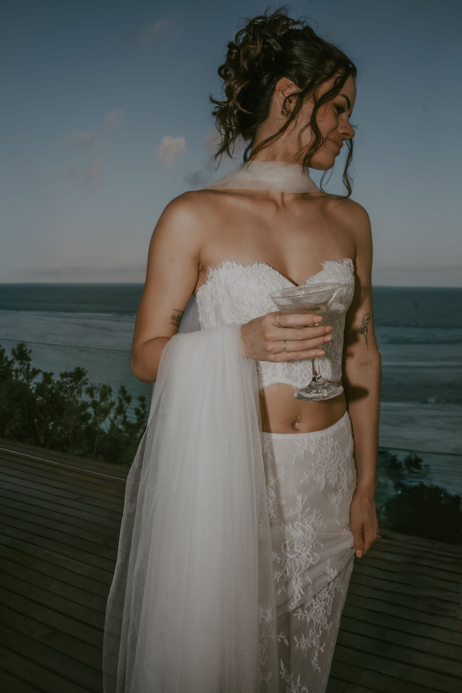 Two brides in white wedding dresses embrace on an oceanfront deck during an intimate seaside ceremony.