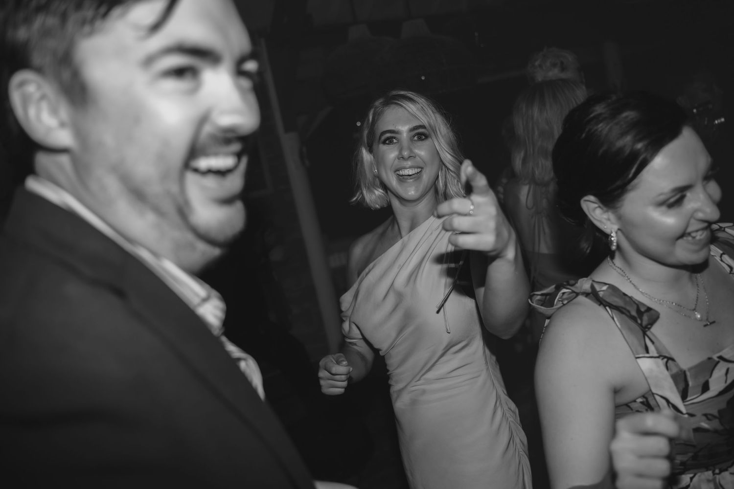 Black and white candid shot of guests enjoying themselves at wedding reception.