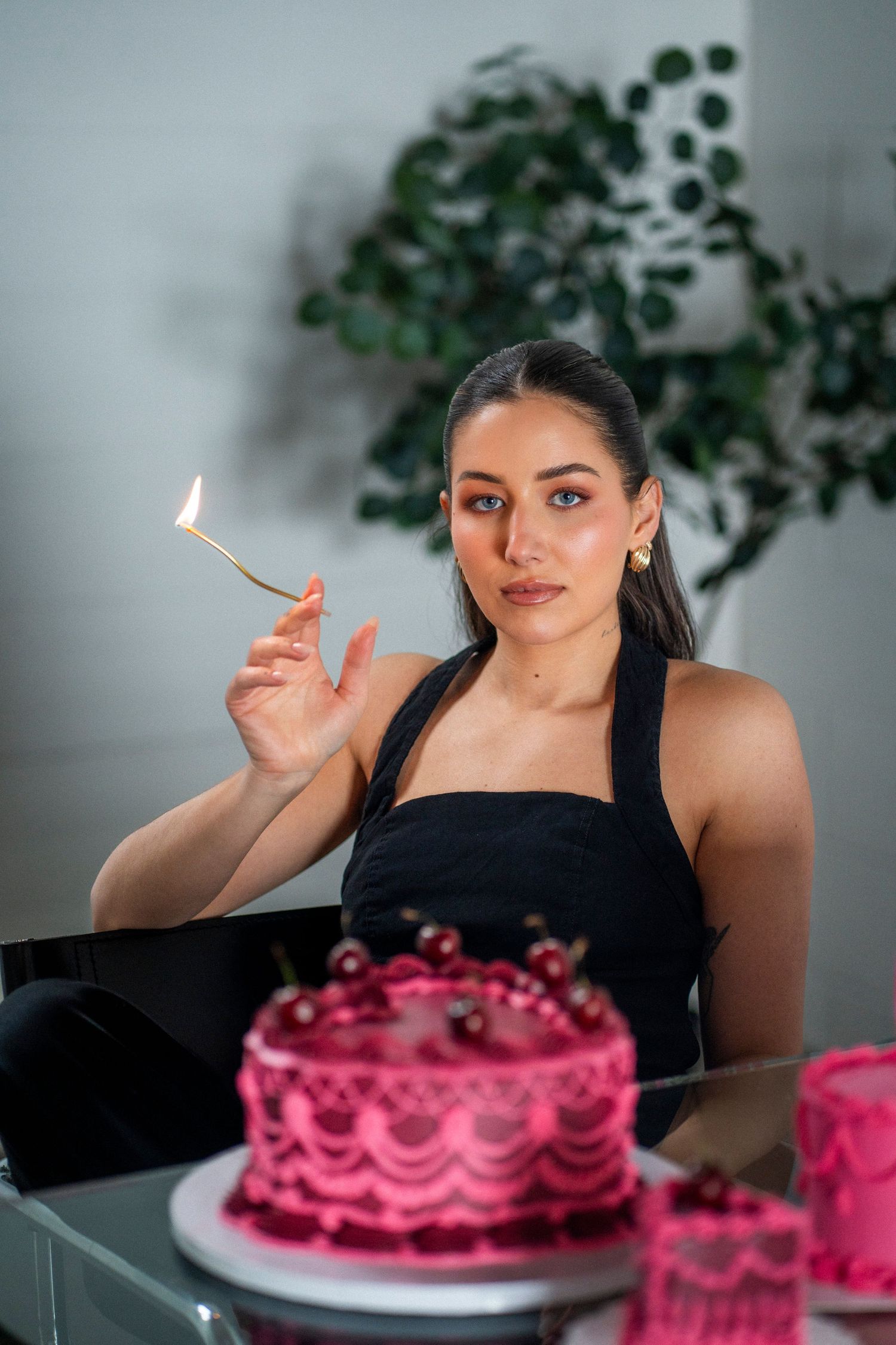 A woman acts like she is smoking a candle, surrounded by pink and maroon cakes.