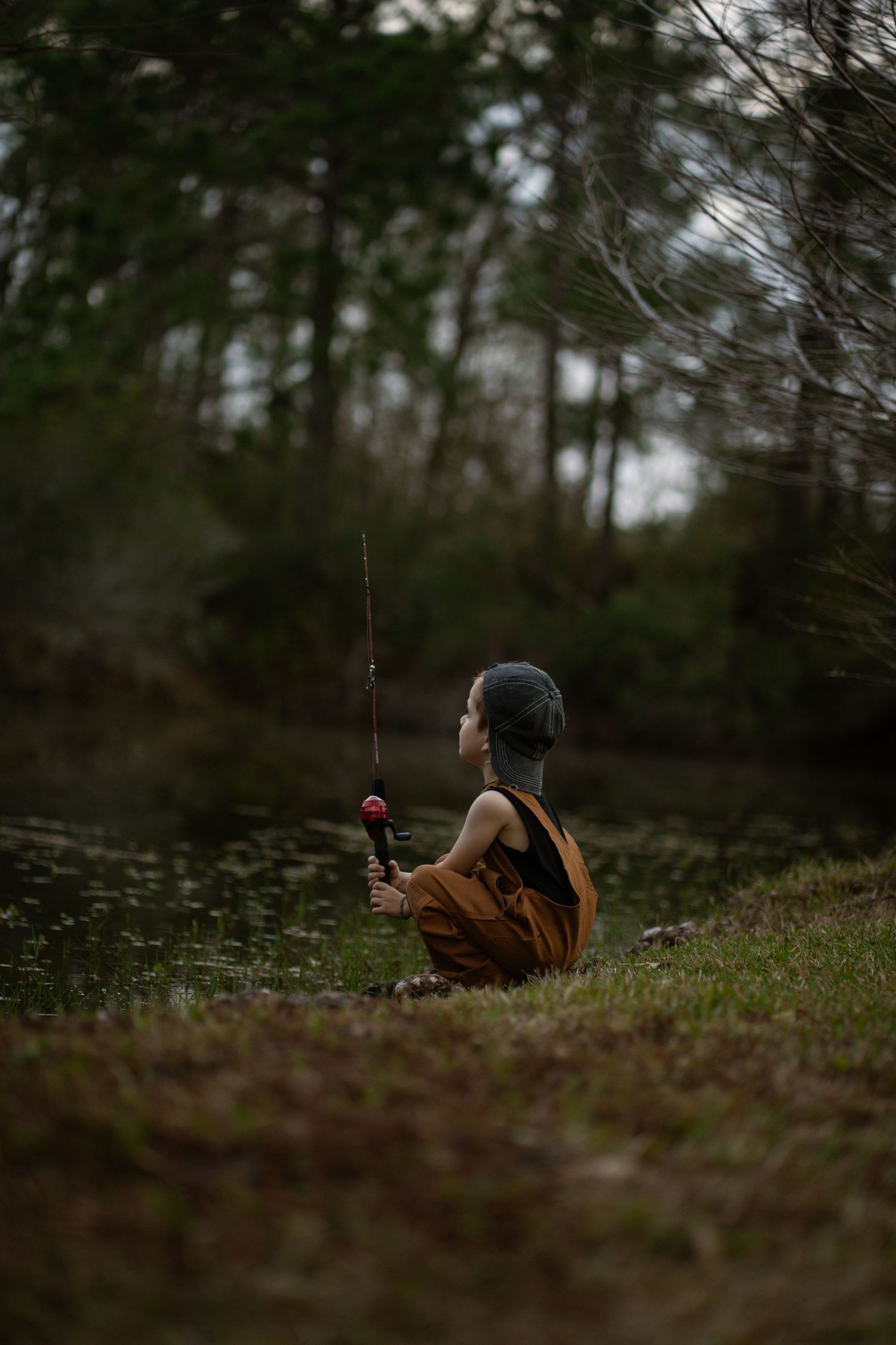 A small boy fishing in overalls.