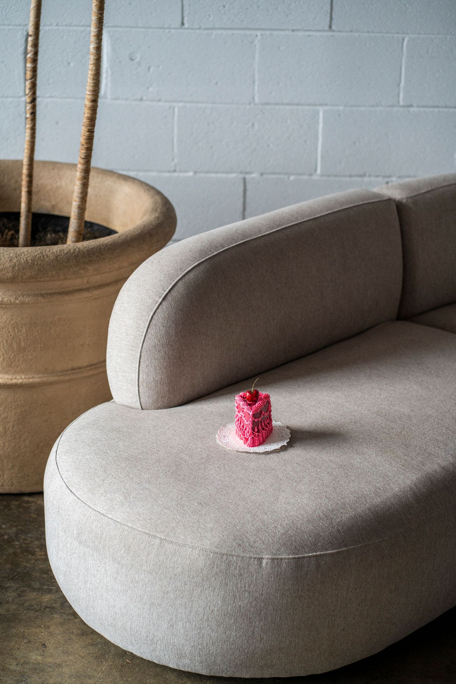 A pink cake slice sits on a white plate on top of a grey couch.