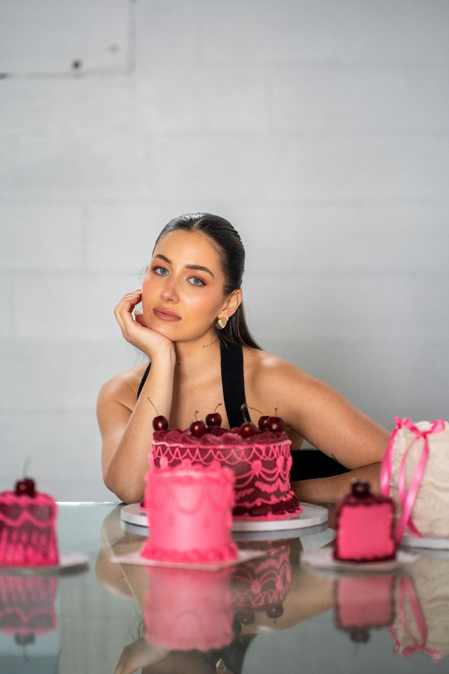 A woman stares at the camera, with one hand supporting her chin, surrounded by hot pink and maroon cakes.