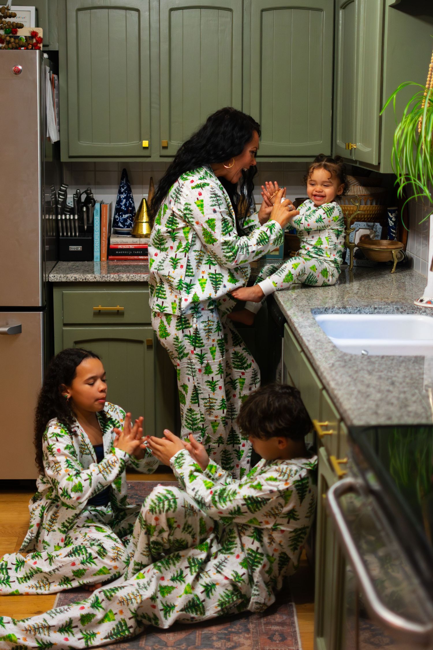 A family in matching pajamas playing patty cake in the kitchen.