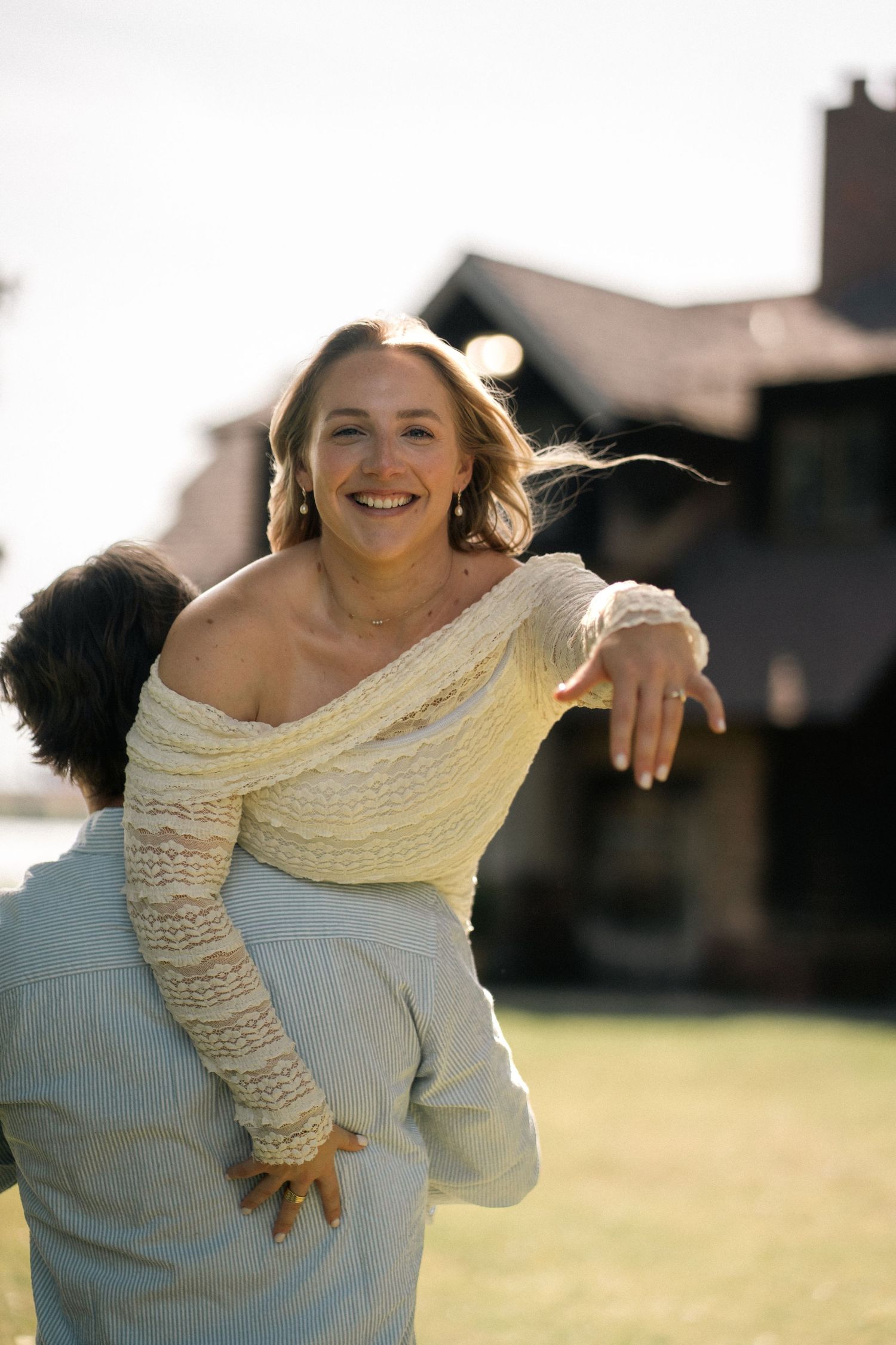 A joyful woman in an off-shoulder yellow top laughs while being lifted by her partner outdoors.