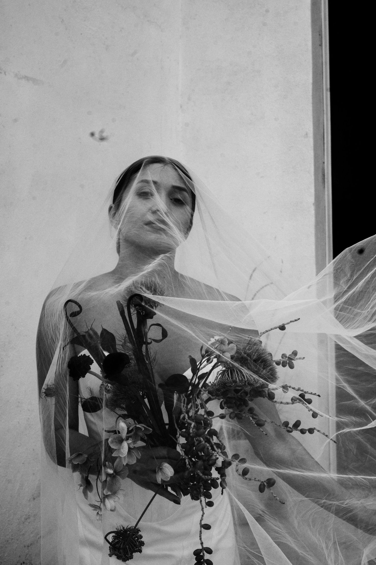 A bride holding a bunch of flowers with a duster veil flowing in the wind in front of her face