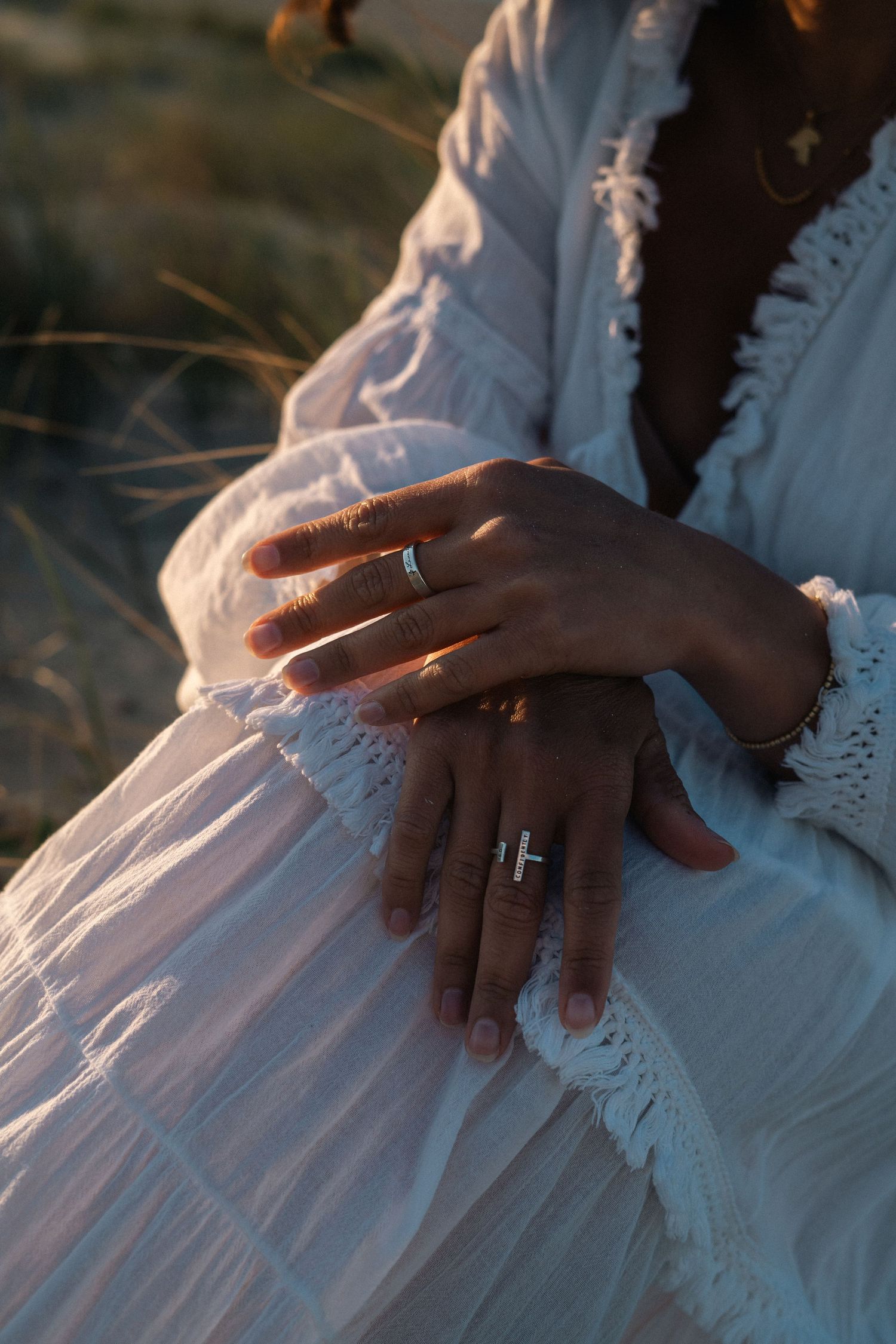 Close-up of a woman's hands adorned with silver rings wearing a flowing white boho lace dress at golden hour.