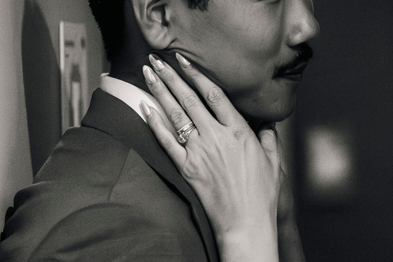 Black and white photo of a couple embracing, woman's hand with diamond ring resting on man's jaw.