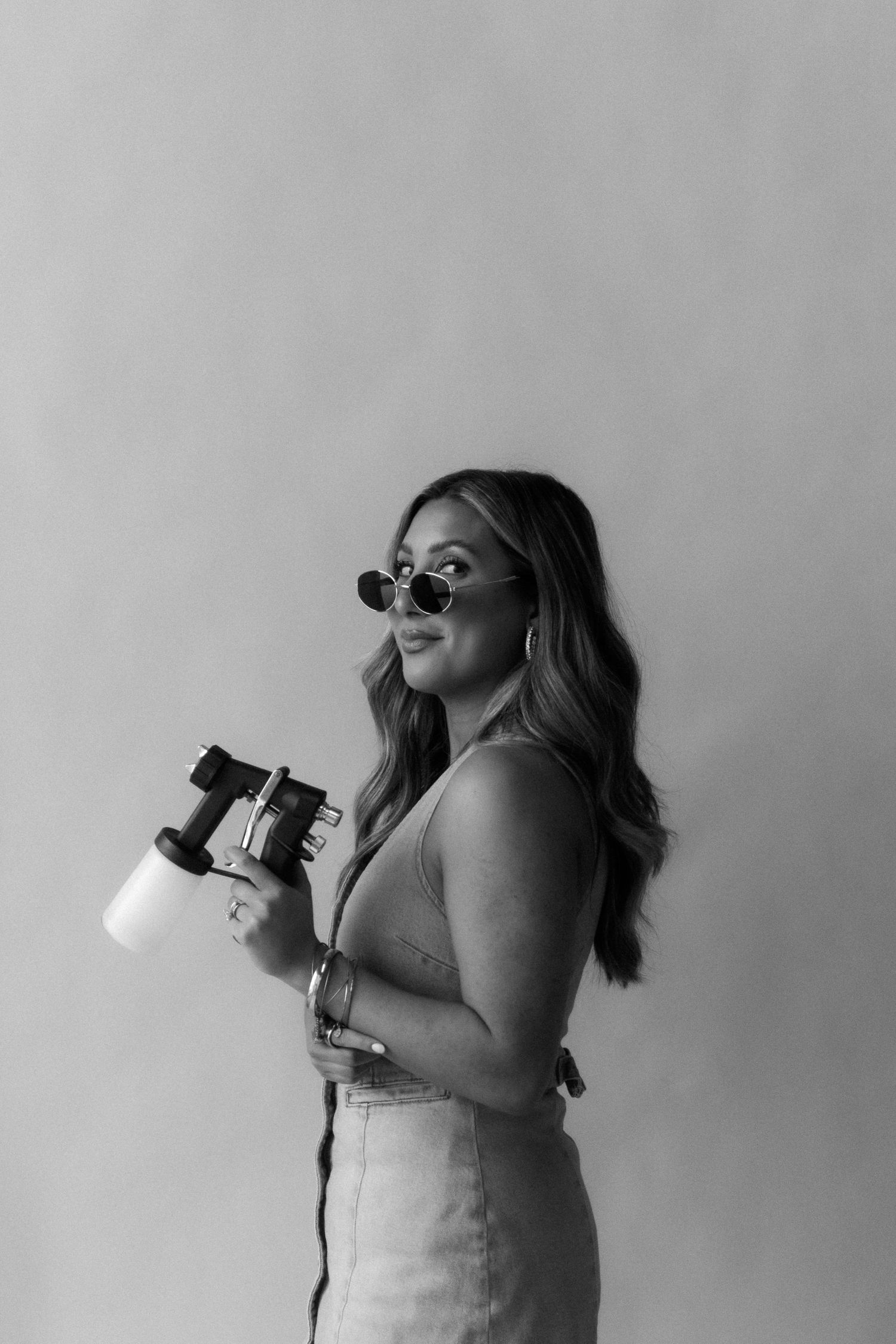 A woman with sunglasses on holding a spray tan gun.