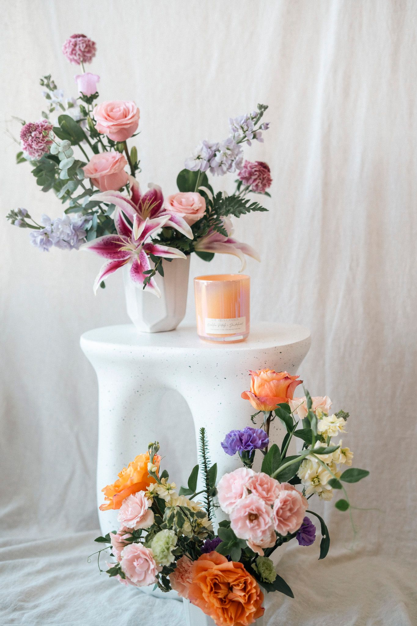 Colorful floral arrangement with pink roses and lilies on white pedestal table with candle.