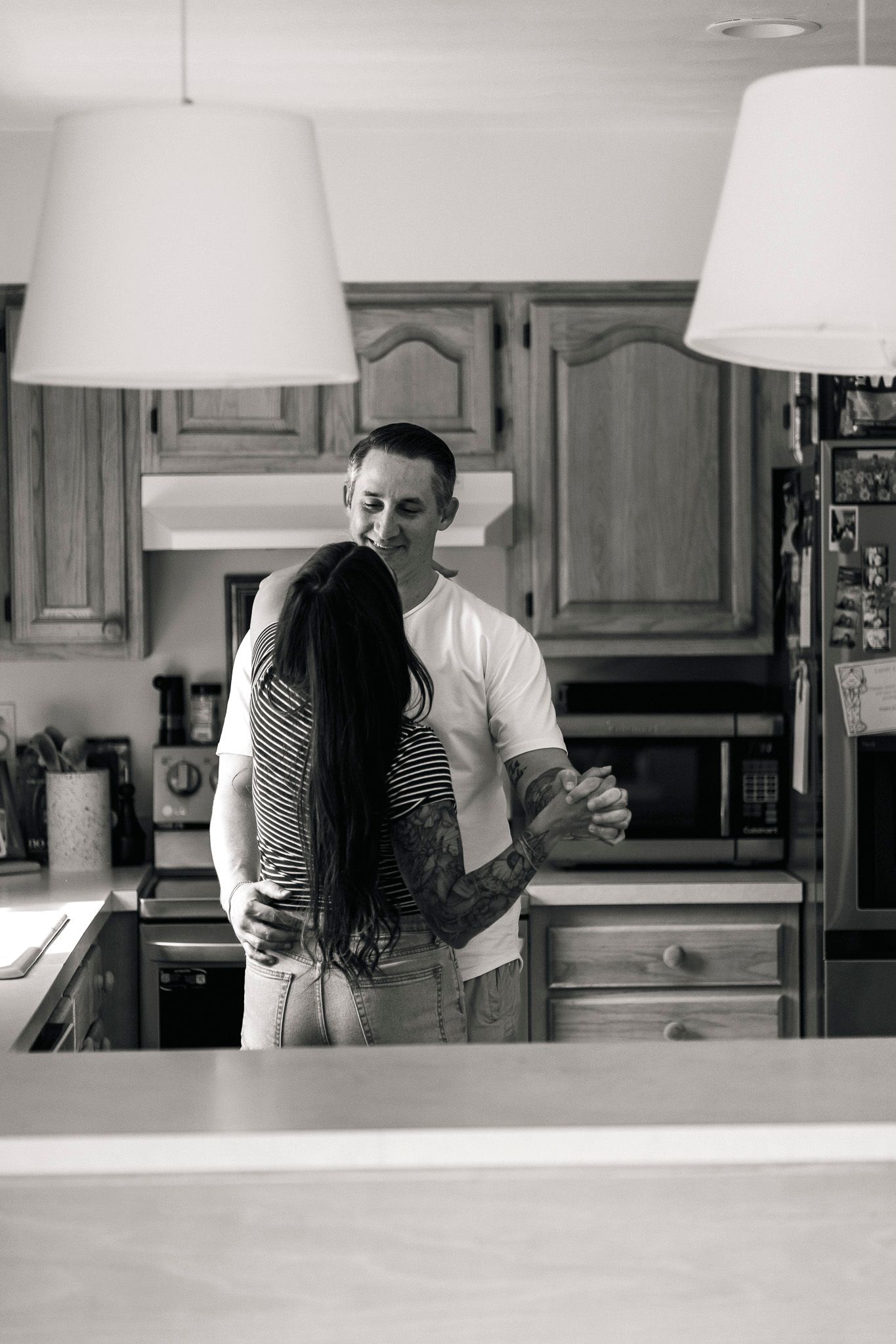 Black and white photo of tattooed couple dancing together in a home kitchen.