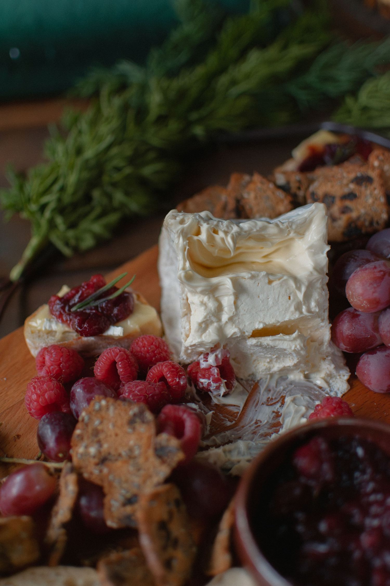 Cheese and fruit with greenery on a charcuterie board.