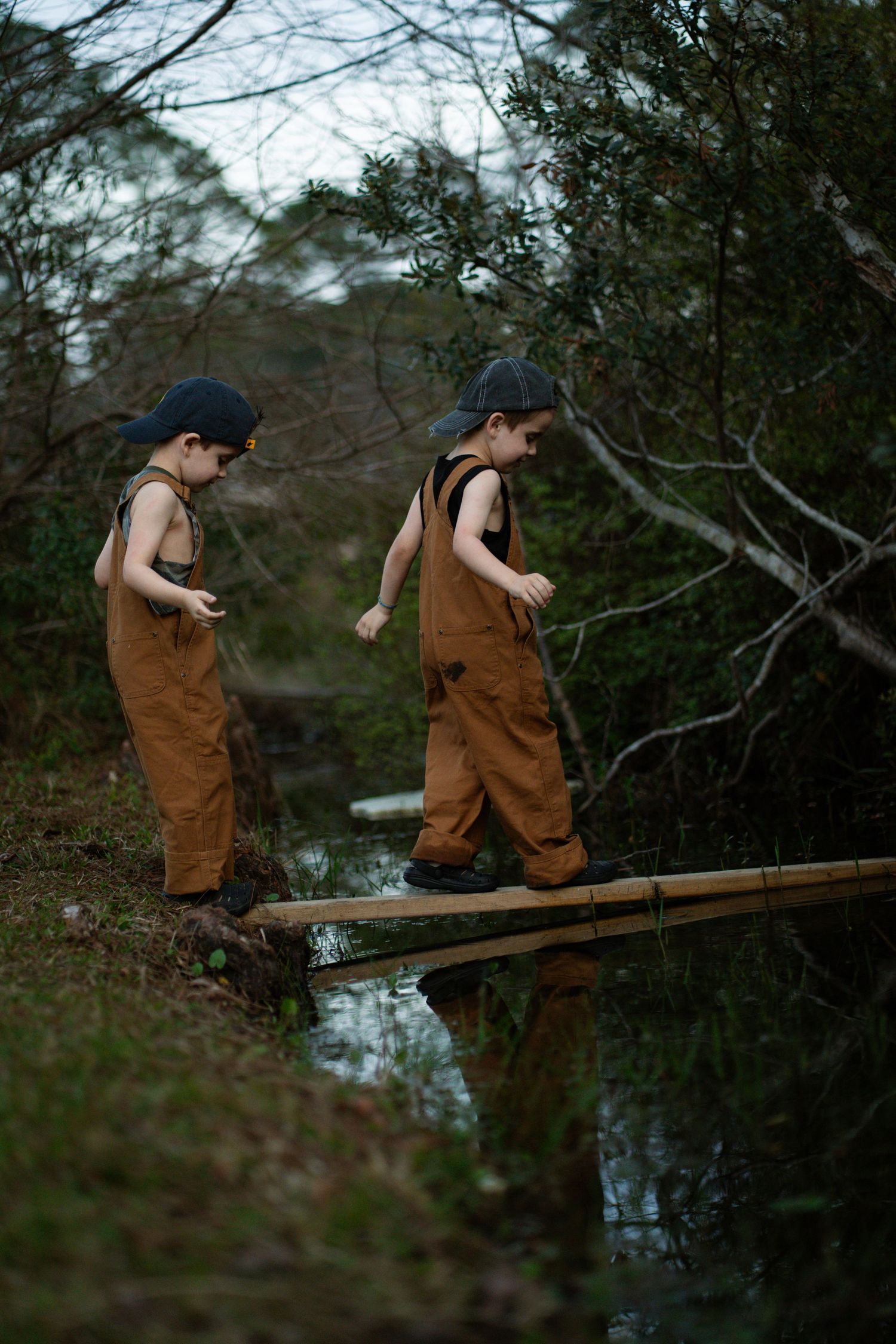Twin boys crossing a stream with a makeshift bridge.