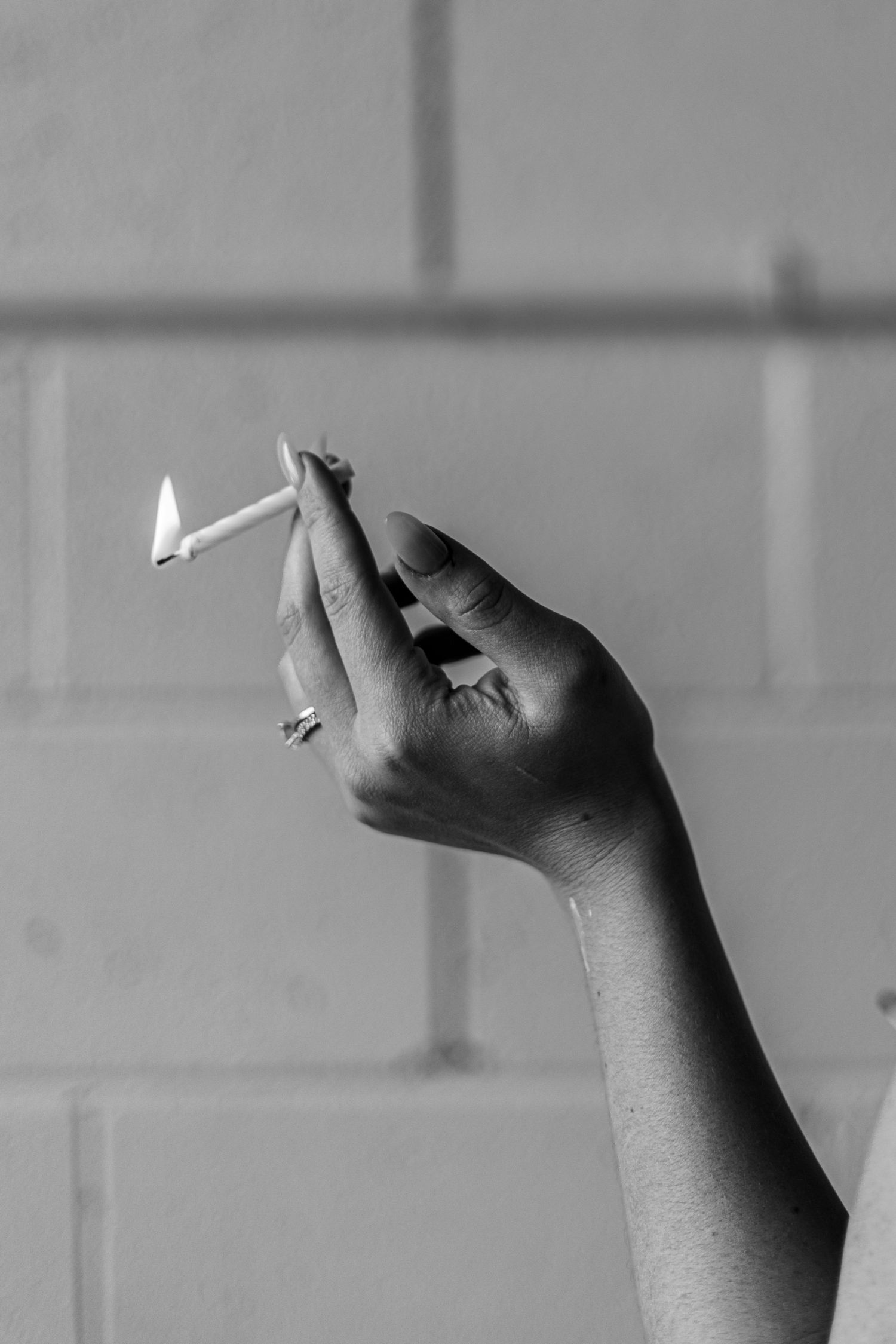 Black and white photo of a hand holding a lit match against a brick wall background.