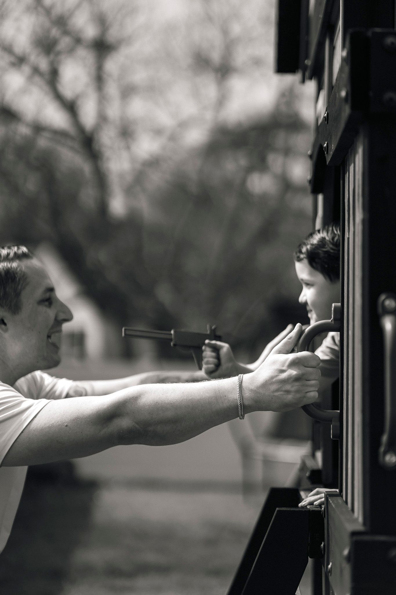 Black and white photo of father and child leaning out of a dark wooden structure outdoors.