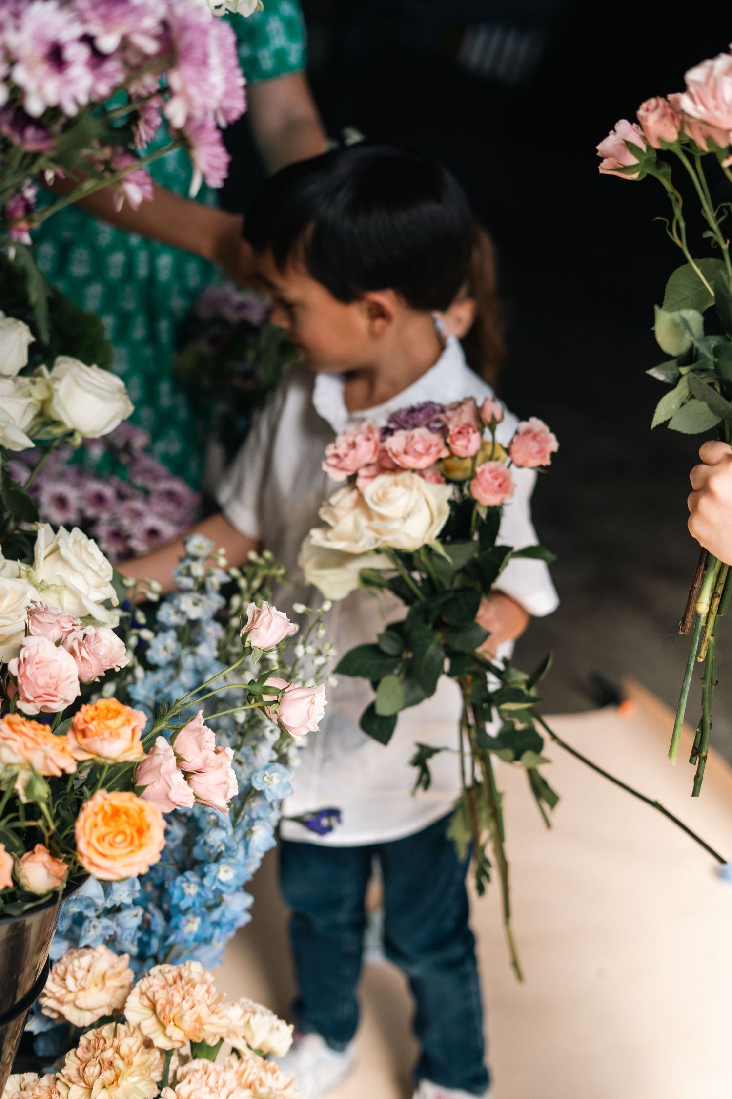 Young child holding pink and white roses at a colorful flower market display.