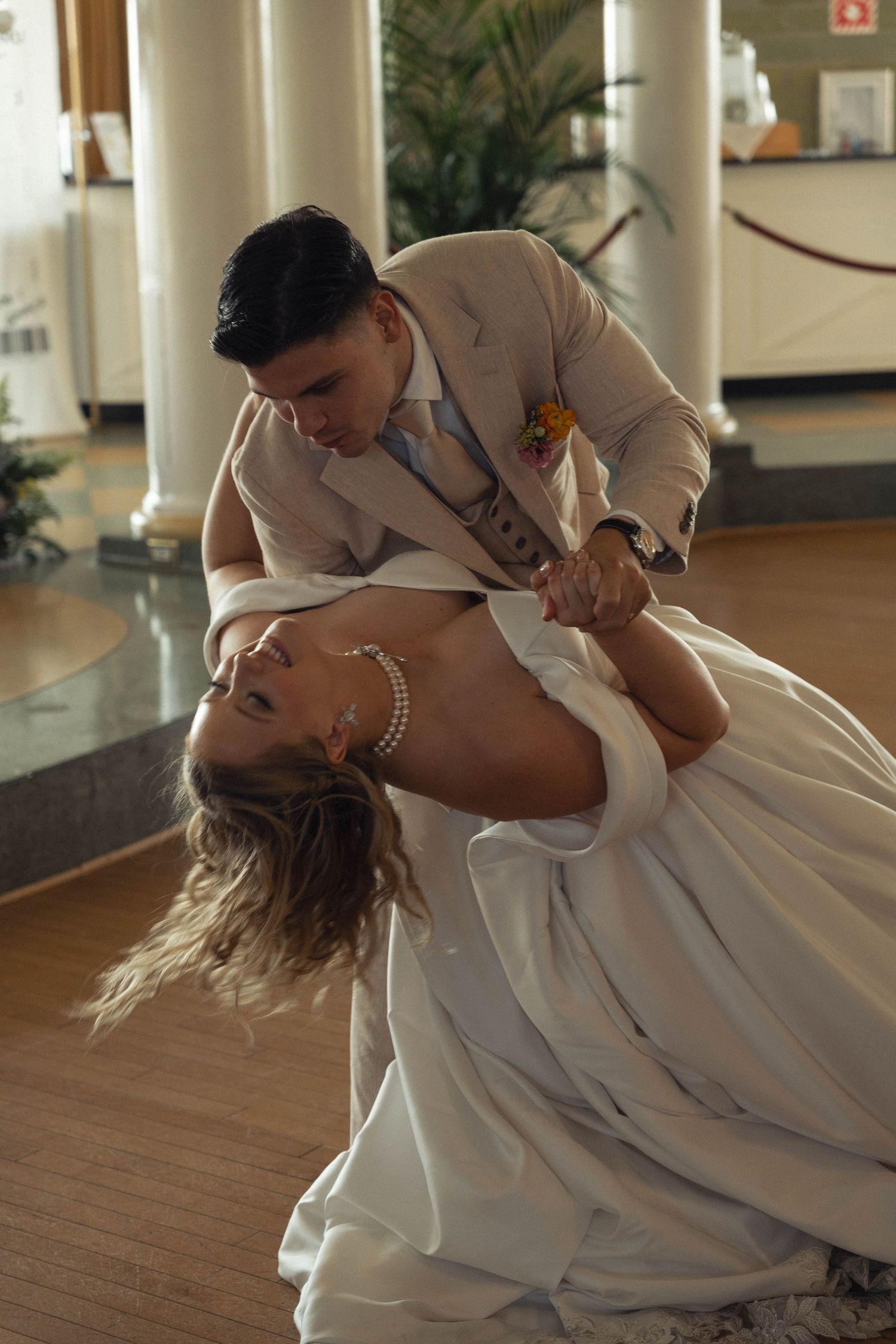 A couple performs a romantic dip dance move on a wooden floor in an elegant setting.