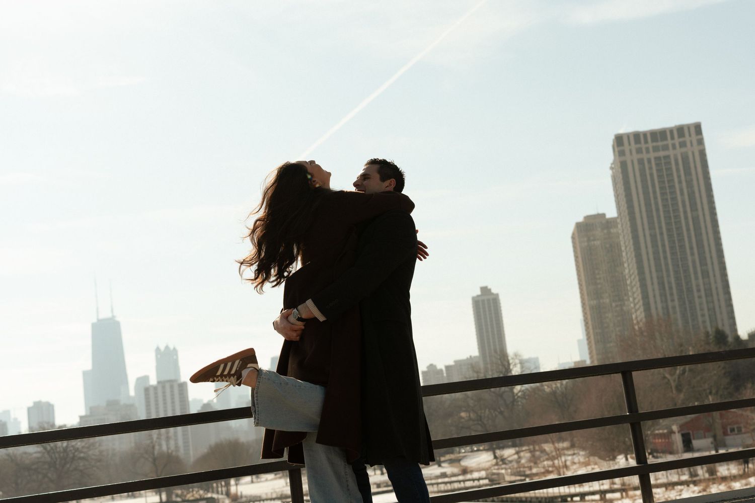 Silhouetted couple embracing on rooftop with Chicago skyline in background during sunset.